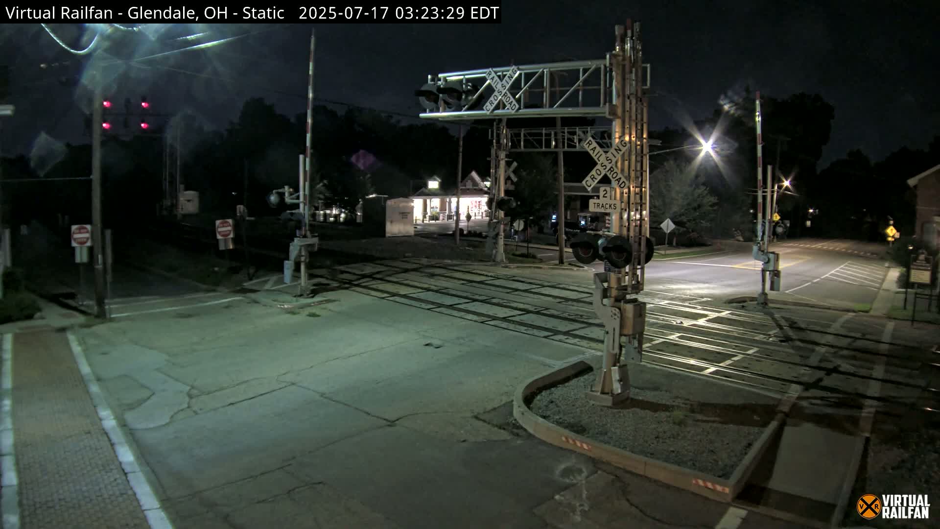 A nighttime view of a deserted railroad crossing with its gates down, illuminated by streetlights.