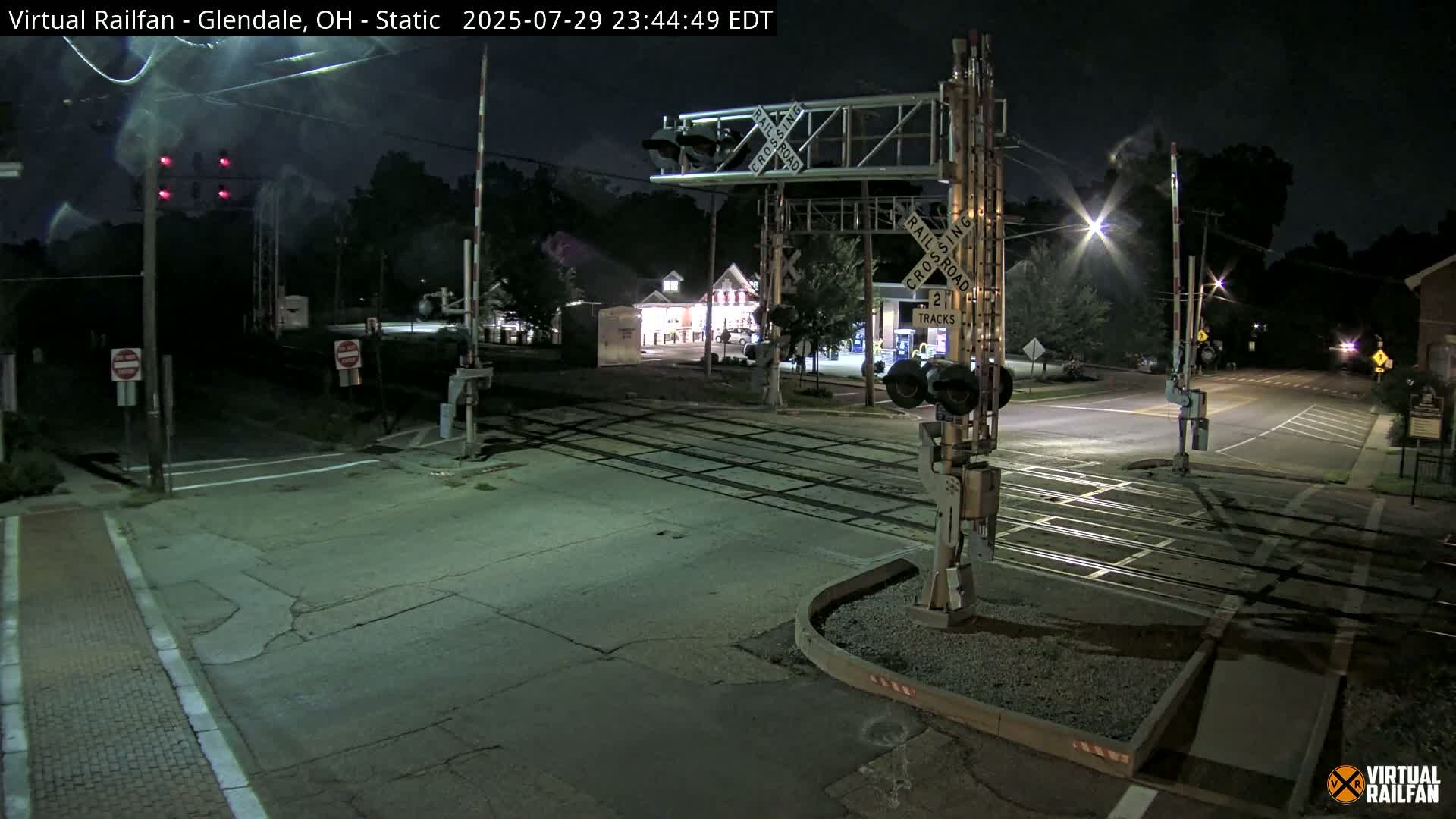 A wet, nighttime view of a railroad crossing with its gates down and red signal lights illuminated.
