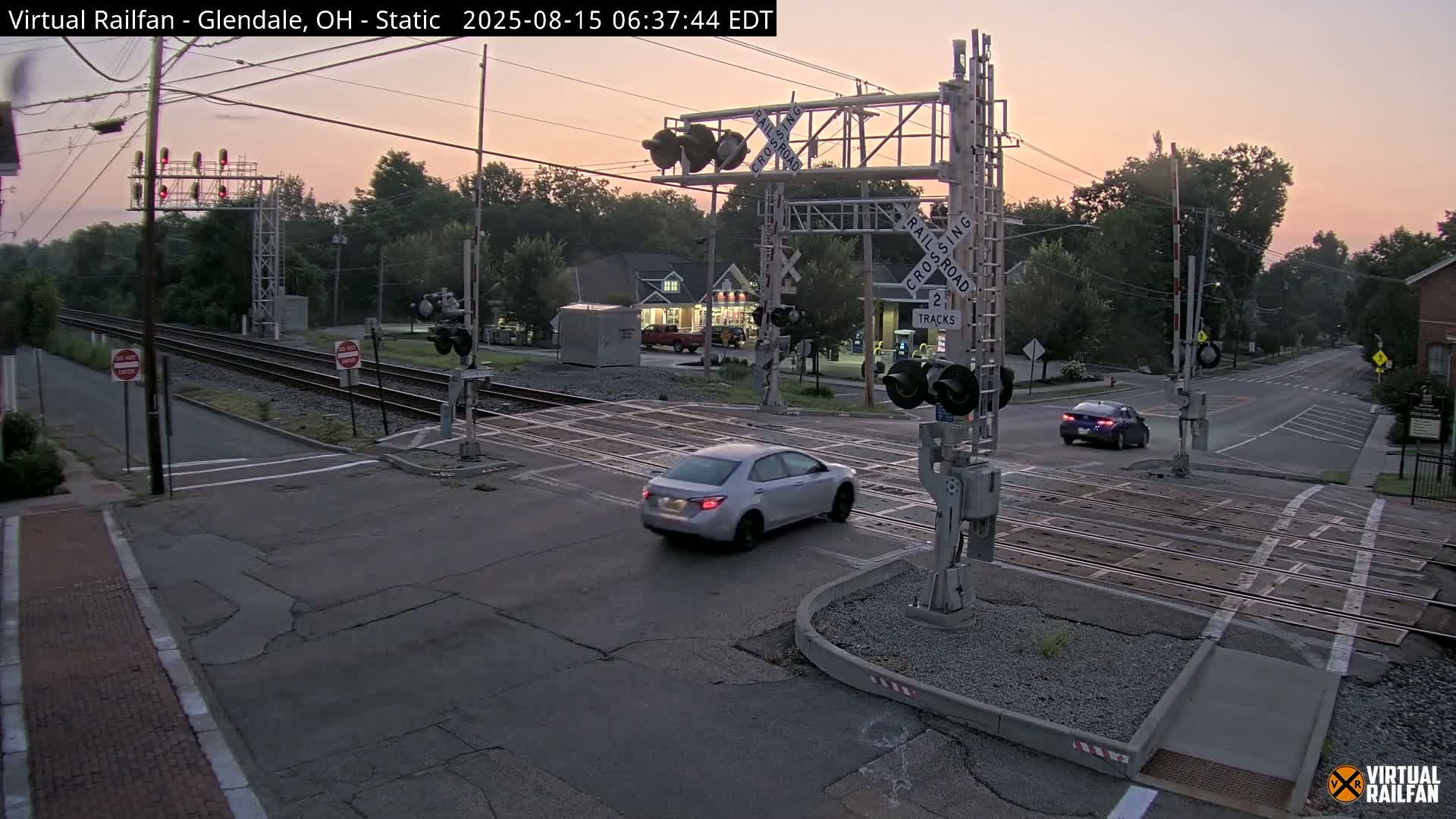 A wet, nighttime view of a railroad crossing with its gates down and red signal lights illuminated.