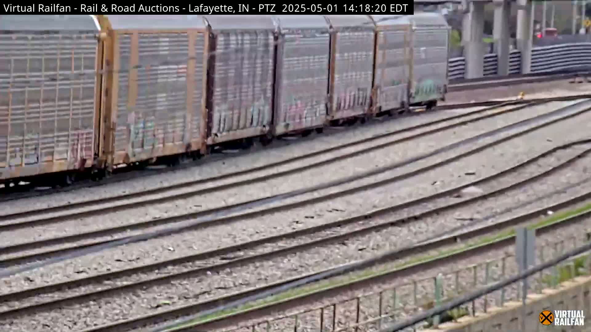 A freight train with graffiti-covered boxcars moves along multiple parallel train tracks on a partly cloudy day.
