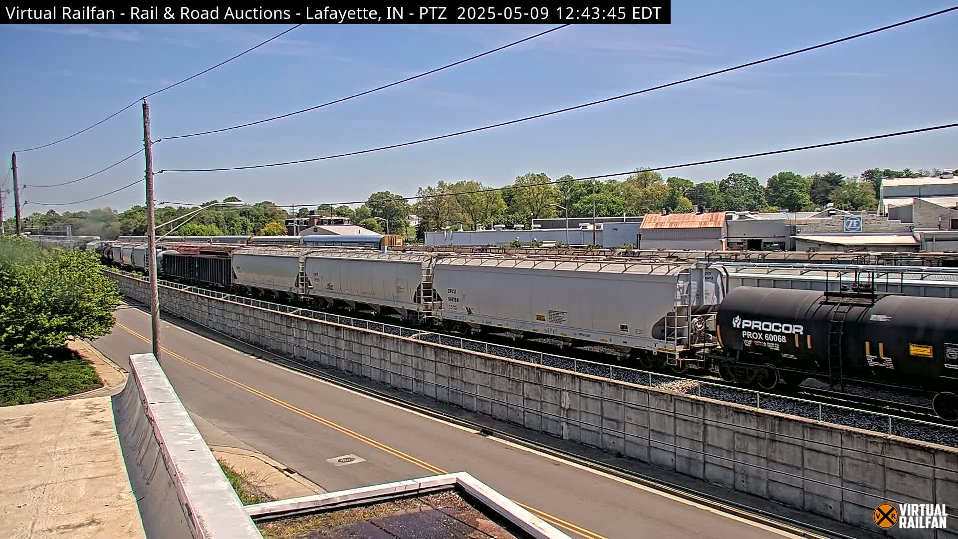 A long freight train passes by a road on a sunny day.