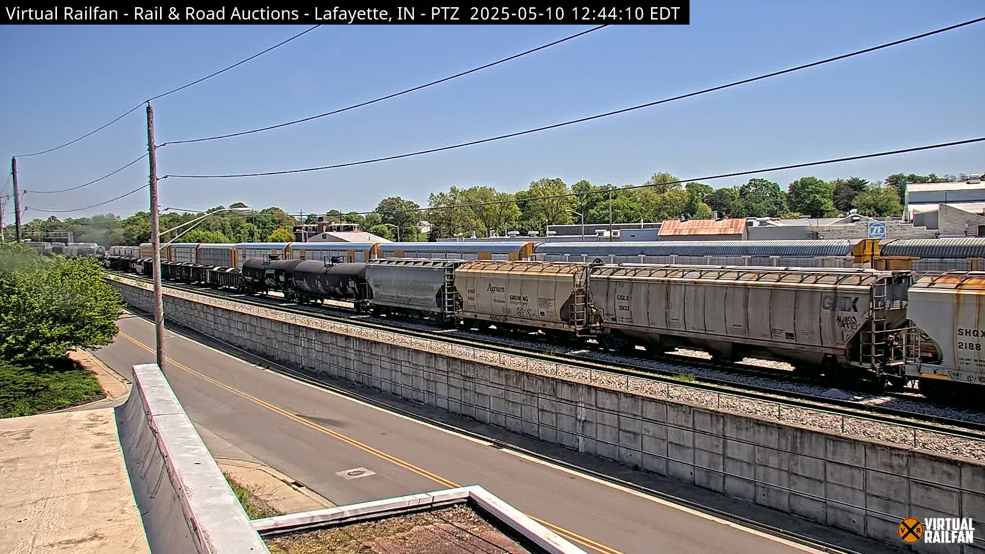 A long freight train is visible on a railway track next to a road under a clear, sunny sky.