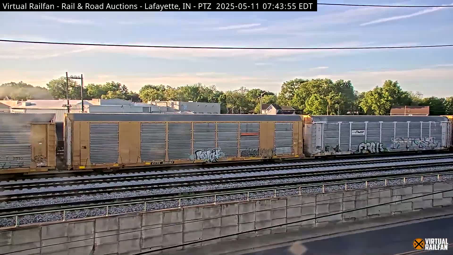 A section of a freight train with graffiti on some of the cars sits on a railway track under a partly cloudy sky.