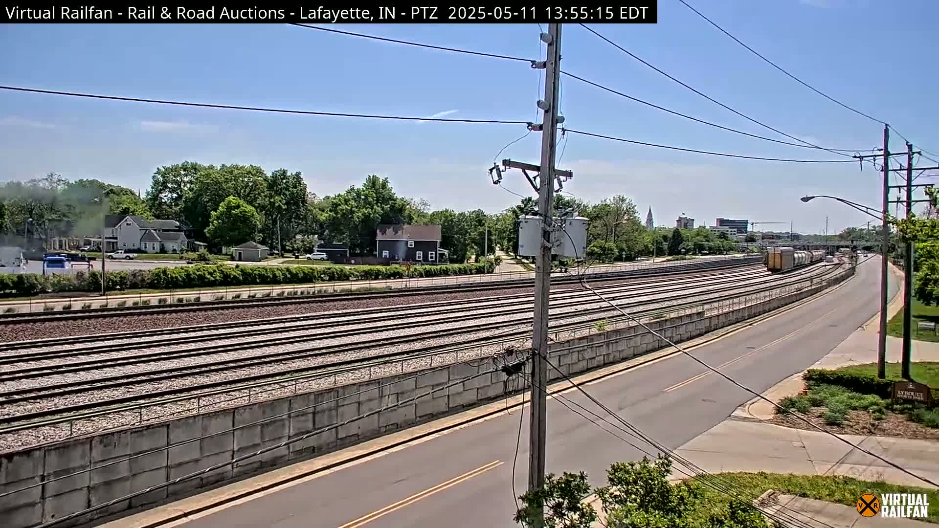 A freight train travels along a set of railway tracks next to a road on a sunny day.