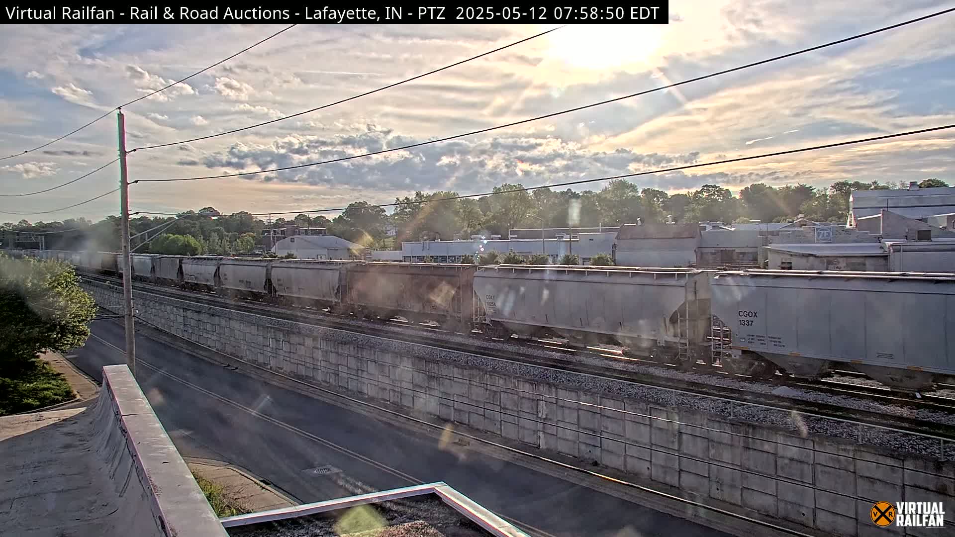 A long freight train passes by on railway tracks next to a road under a partly cloudy sky.