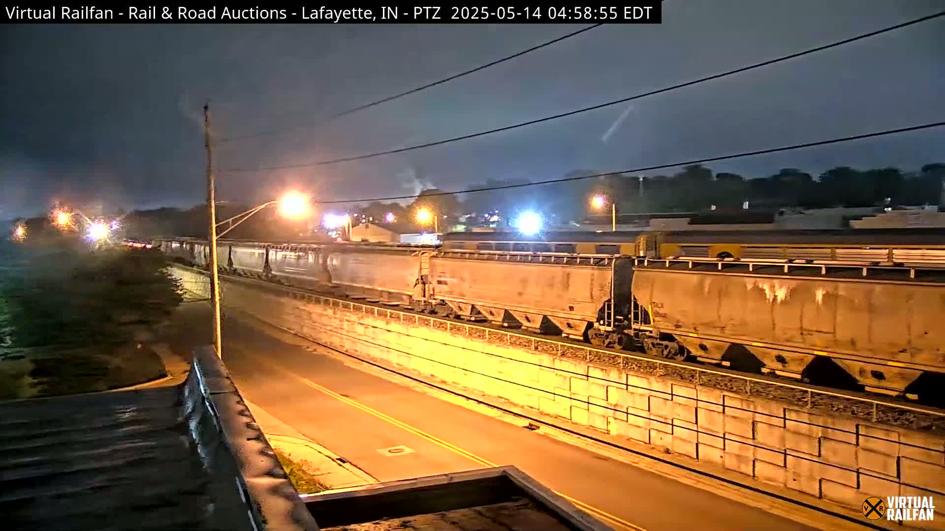 A long freight train passes at night along a wall beside a street under a mostly clear sky.