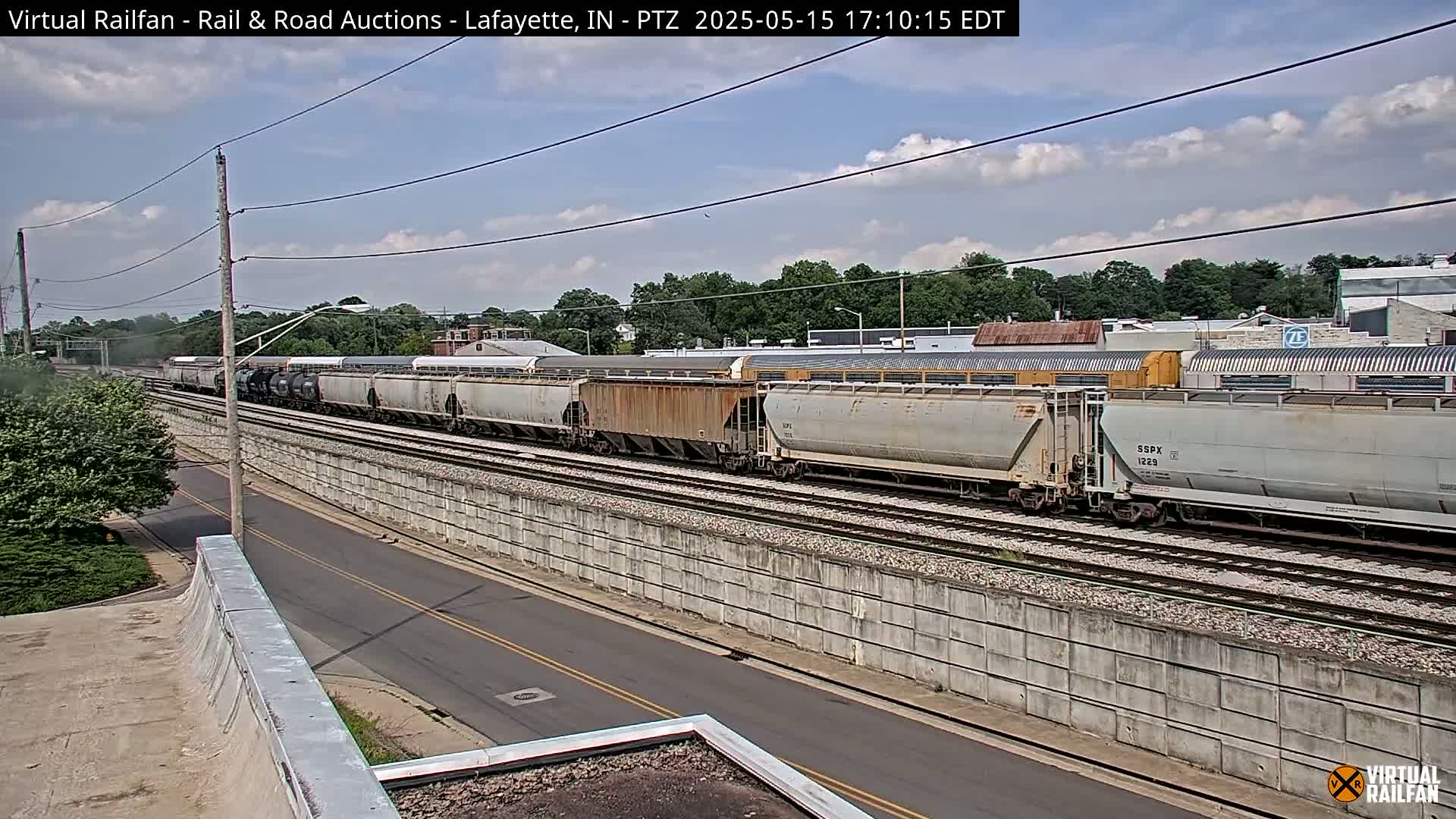 A long freight train passes by a road under a partly cloudy sky.