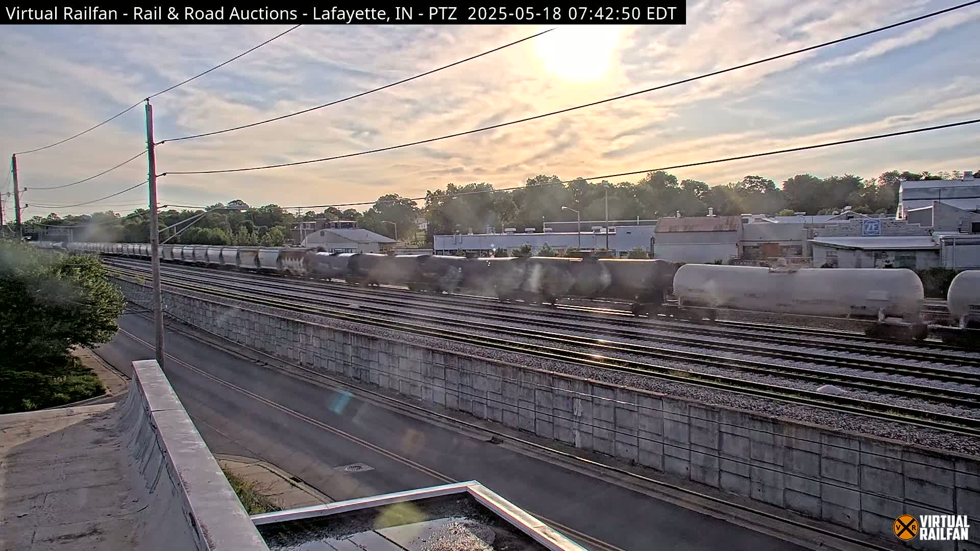 A long freight train passes by under a partly cloudy sunset sky.