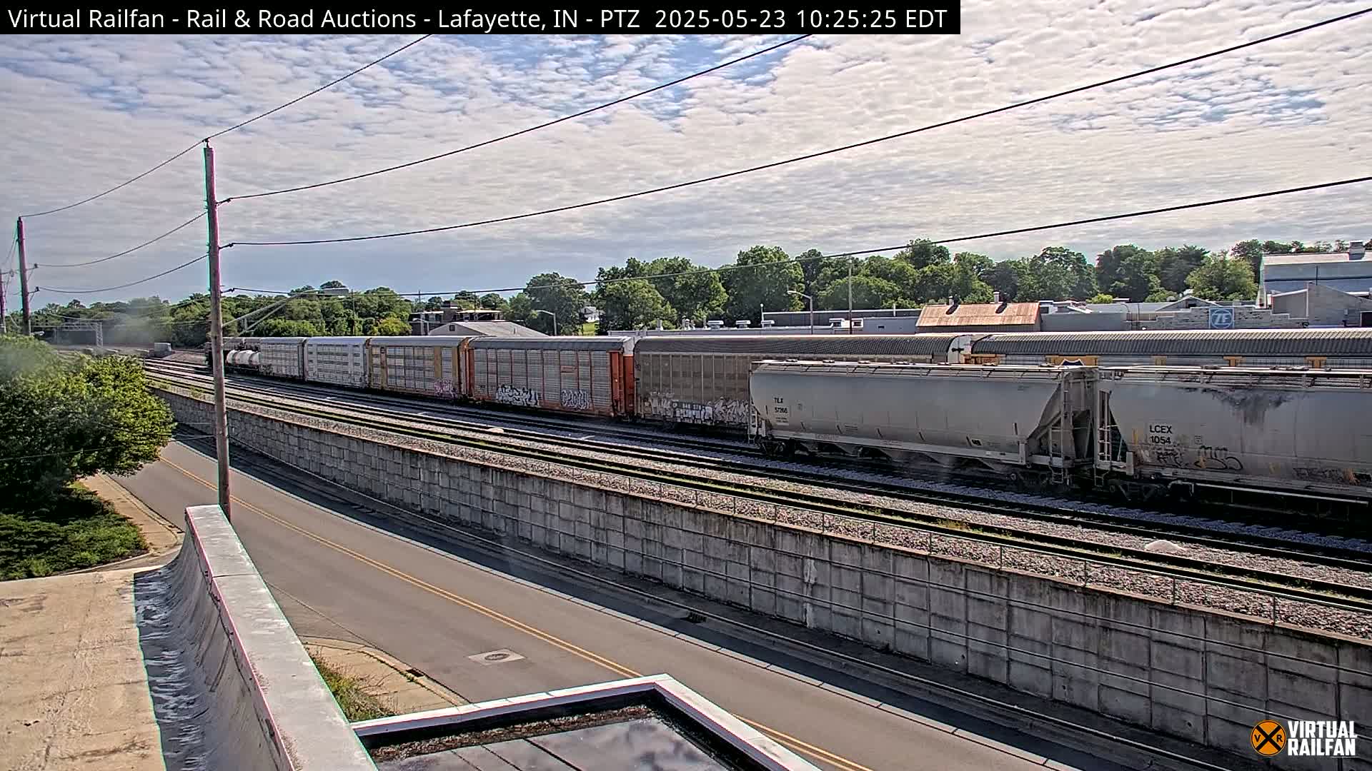 A long freight train passes by on a railway track next to a road under a partly cloudy sky.