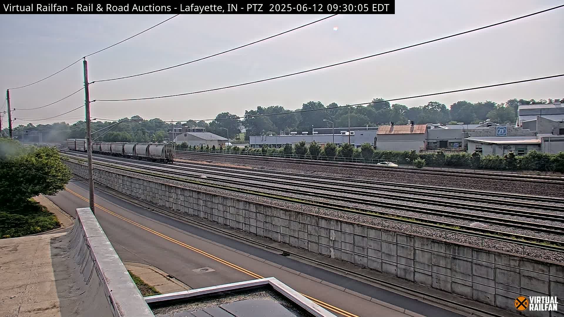 A freight train passes by a roadway and parallel railroad tracks on a partly cloudy day.
