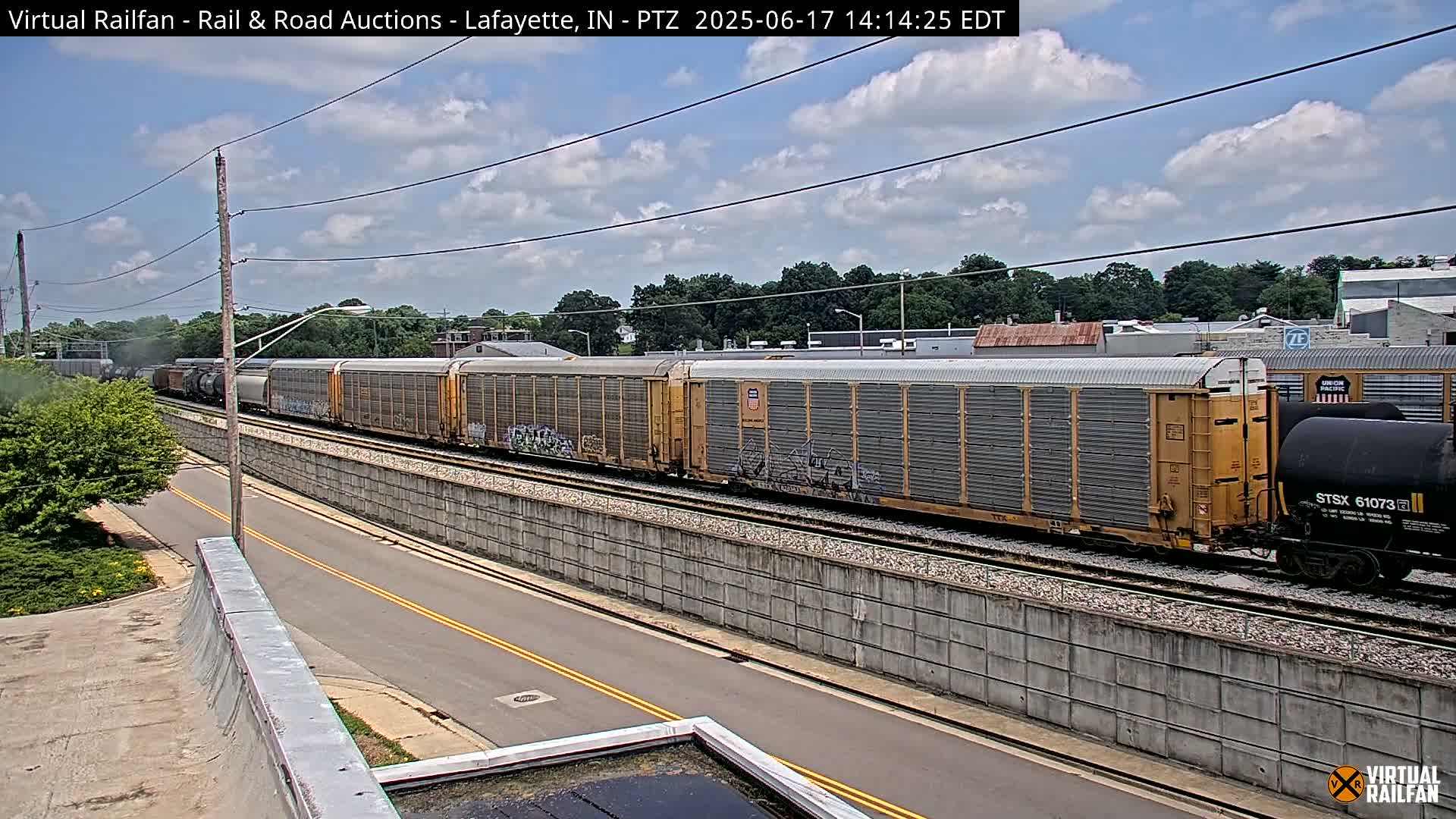 A long freight train passes by a road under a partly cloudy sky.