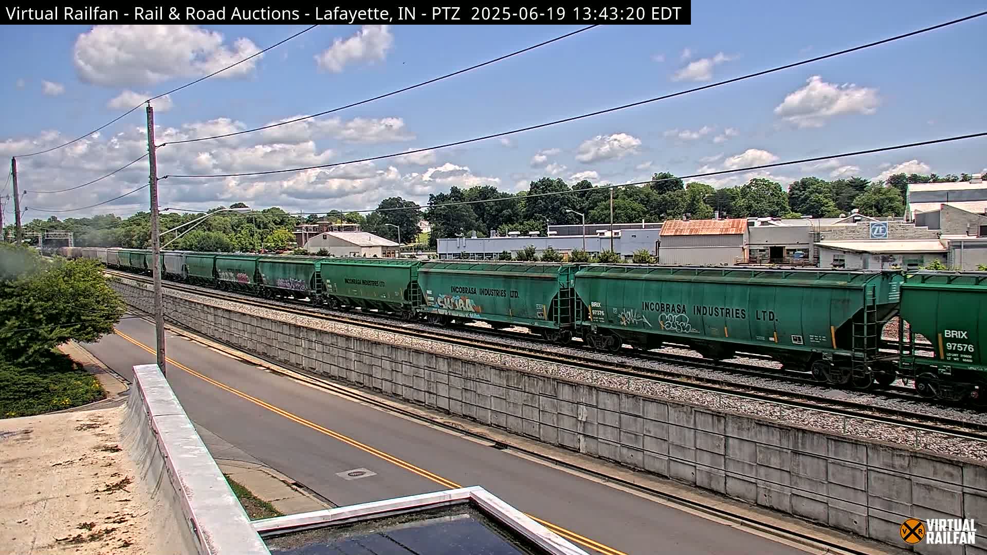 A long freight train of green boxcars travels along railroad tracks under a partly cloudy sky.