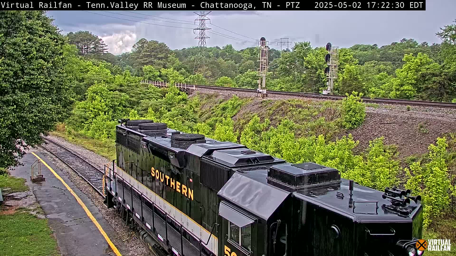 A black Southern Railway locomotive is partially visible on a railway track, surrounded by lush green vegetation under an overcast sky.