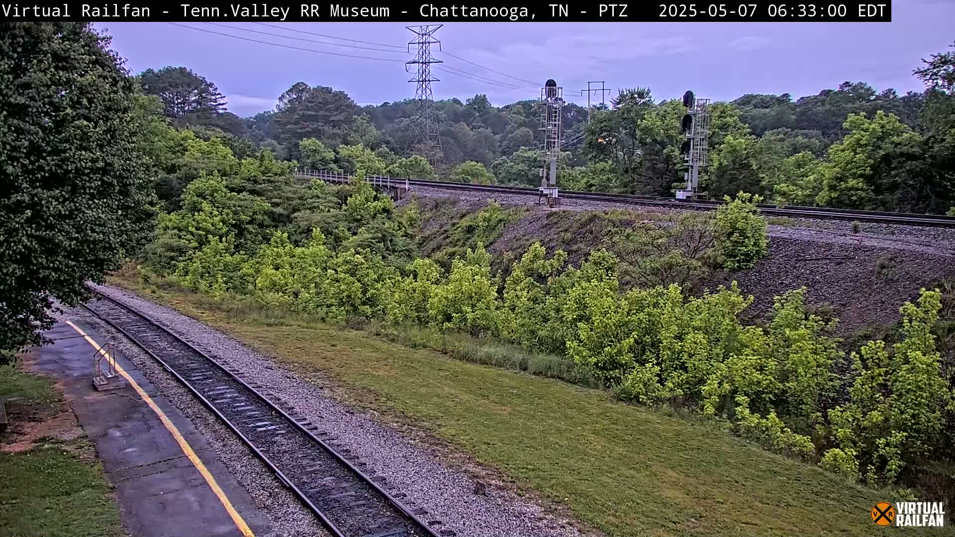 A section of railroad tracks winds through a lush green landscape under an overcast sky.