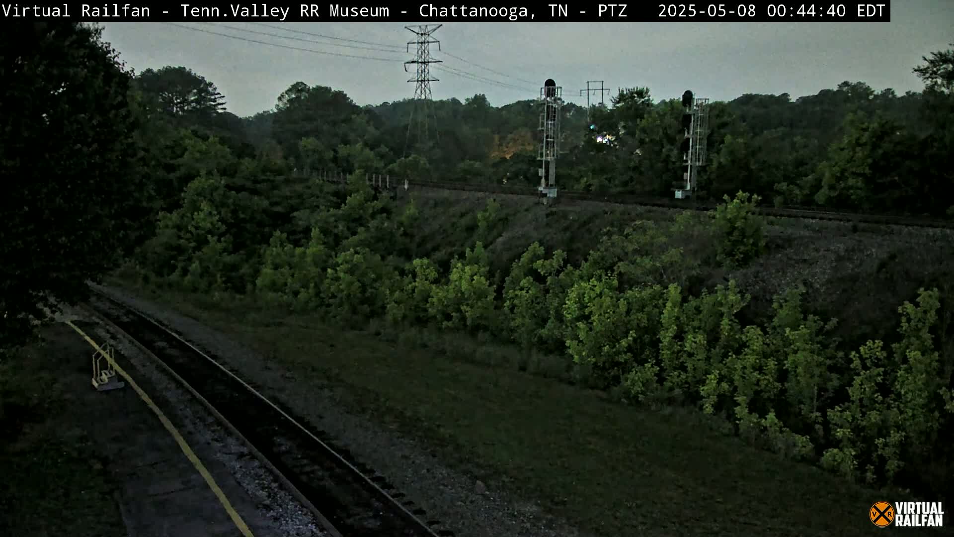 A nighttime view of railroad tracks winding through a lush green landscape under a dusky sky.