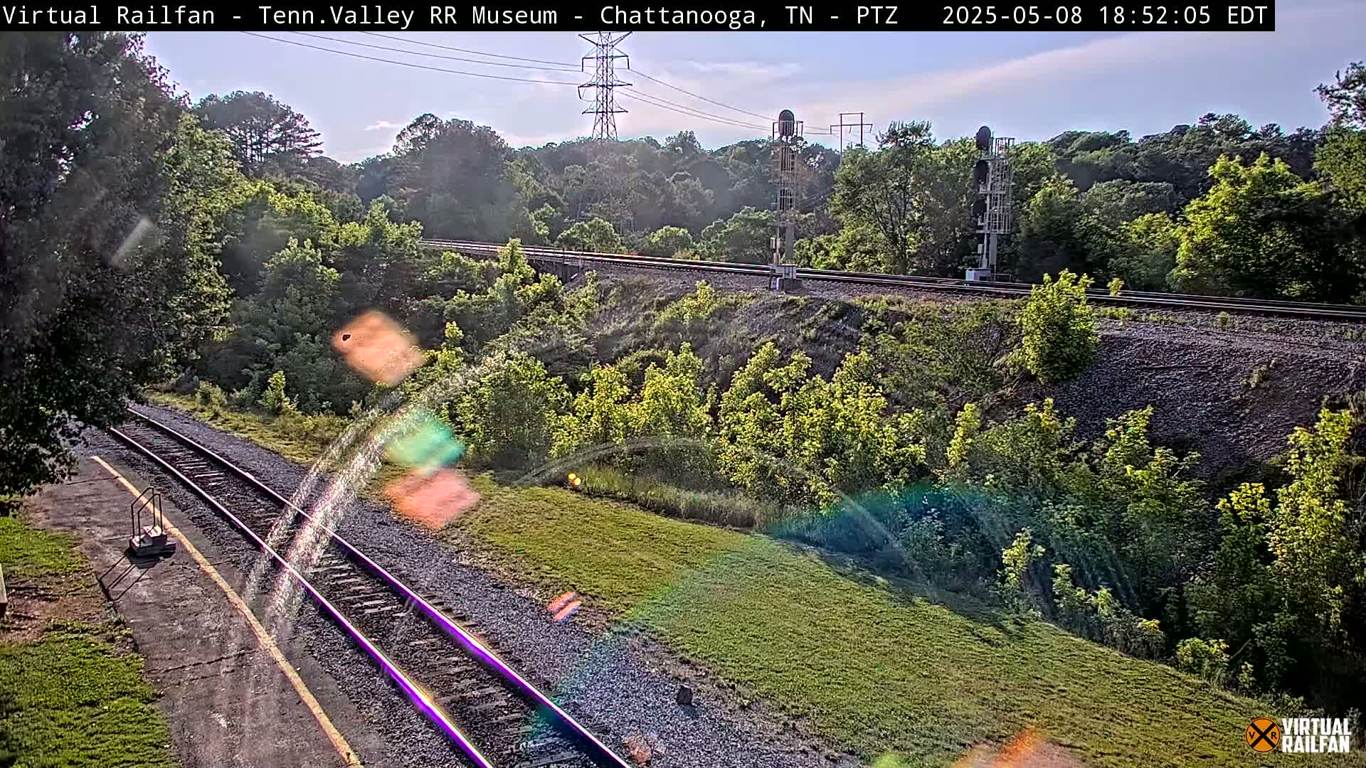 Two sets of train tracks wind through a lush green landscape under a partly sunny sky.