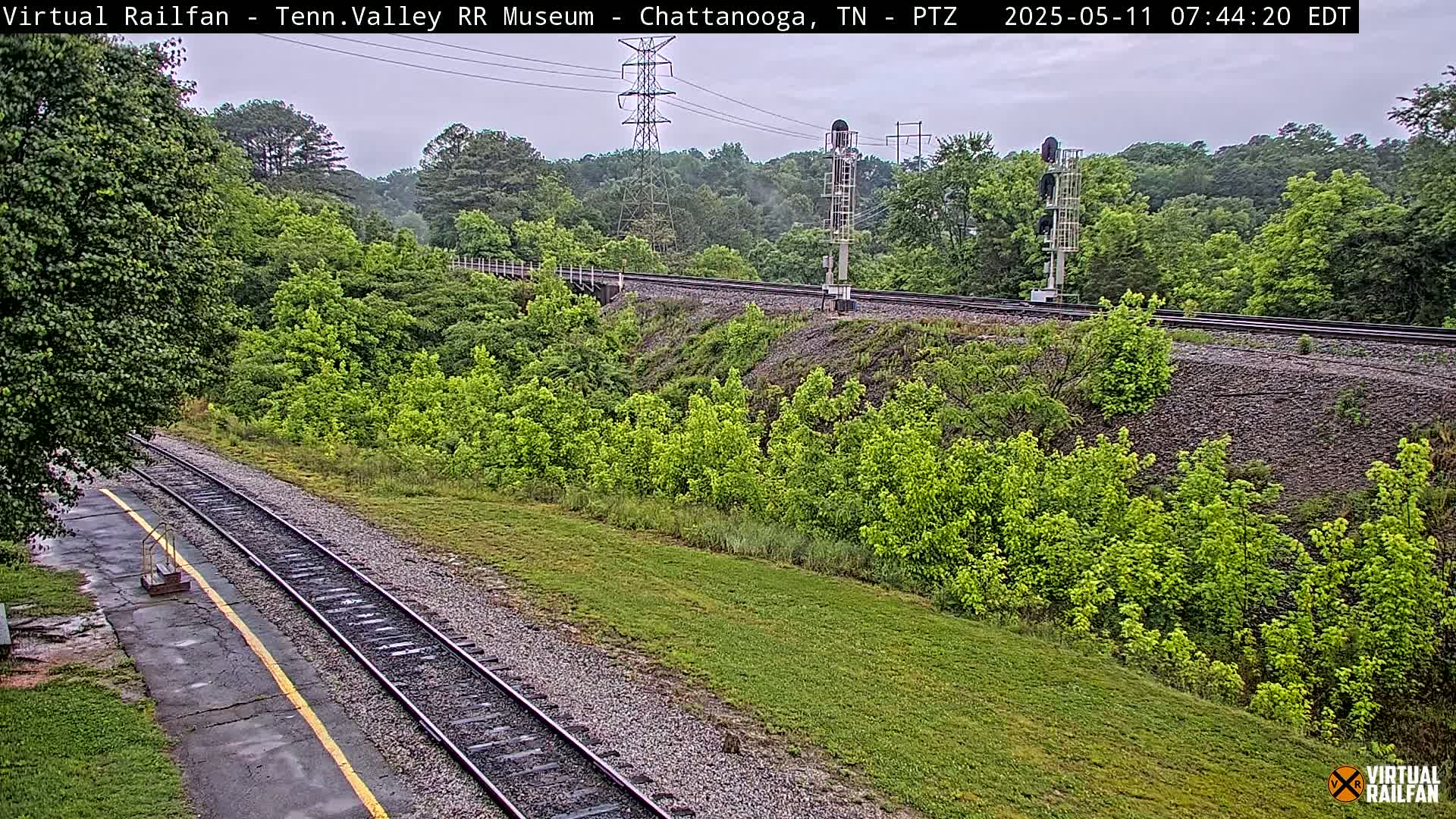 A high-angle view of railroad tracks winding through a lush green landscape under an overcast sky.