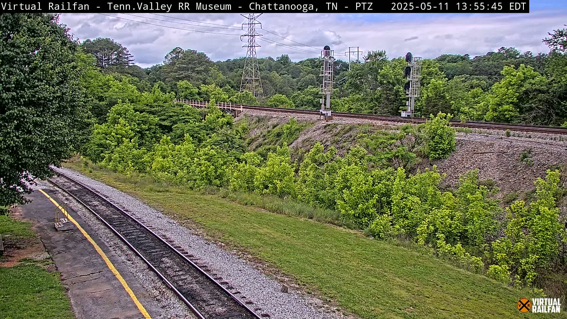 A railroad track winds through a lush green landscape under a partly cloudy sky.