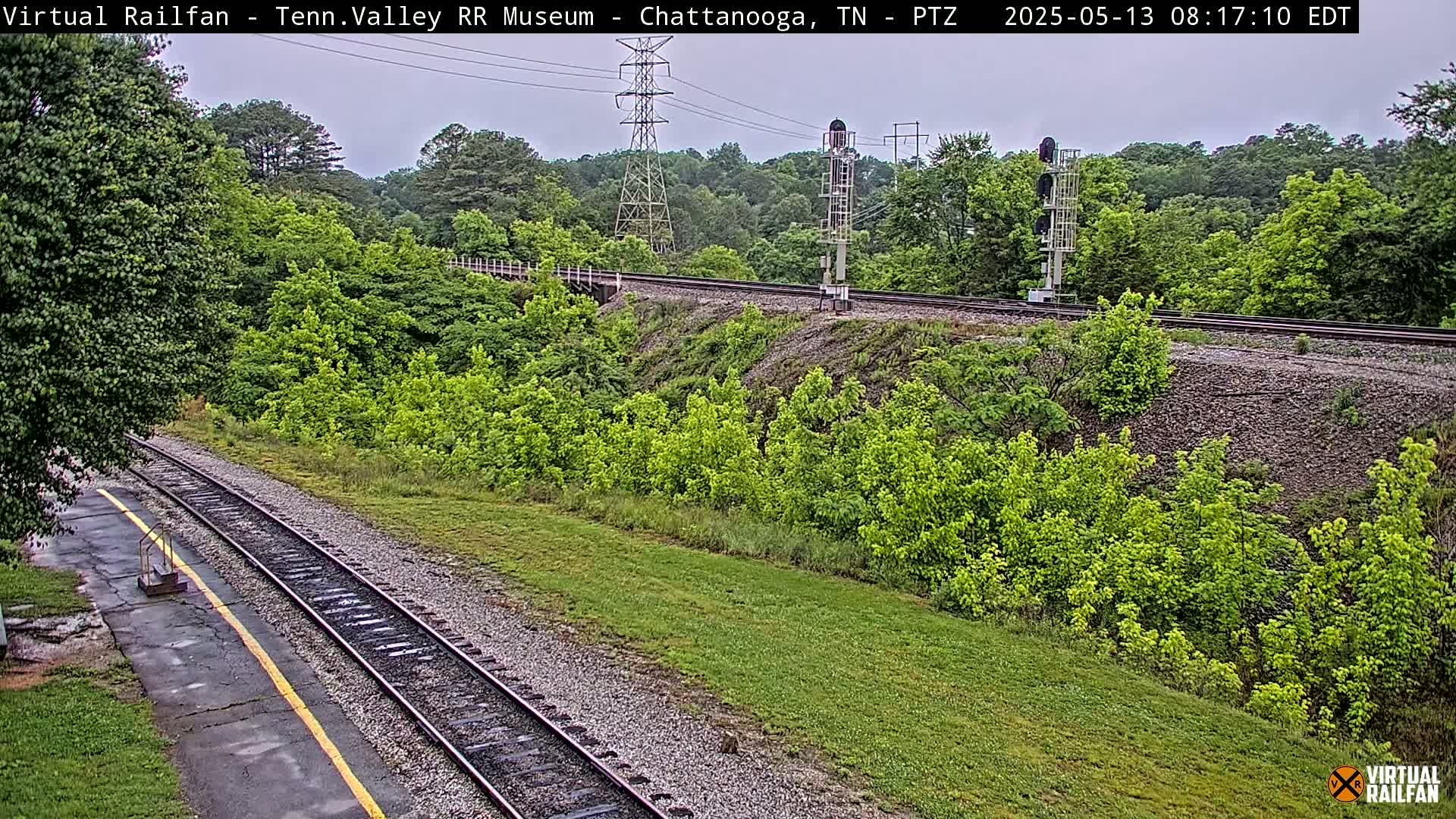 A railroad track curves through a lush green landscape under an overcast sky.