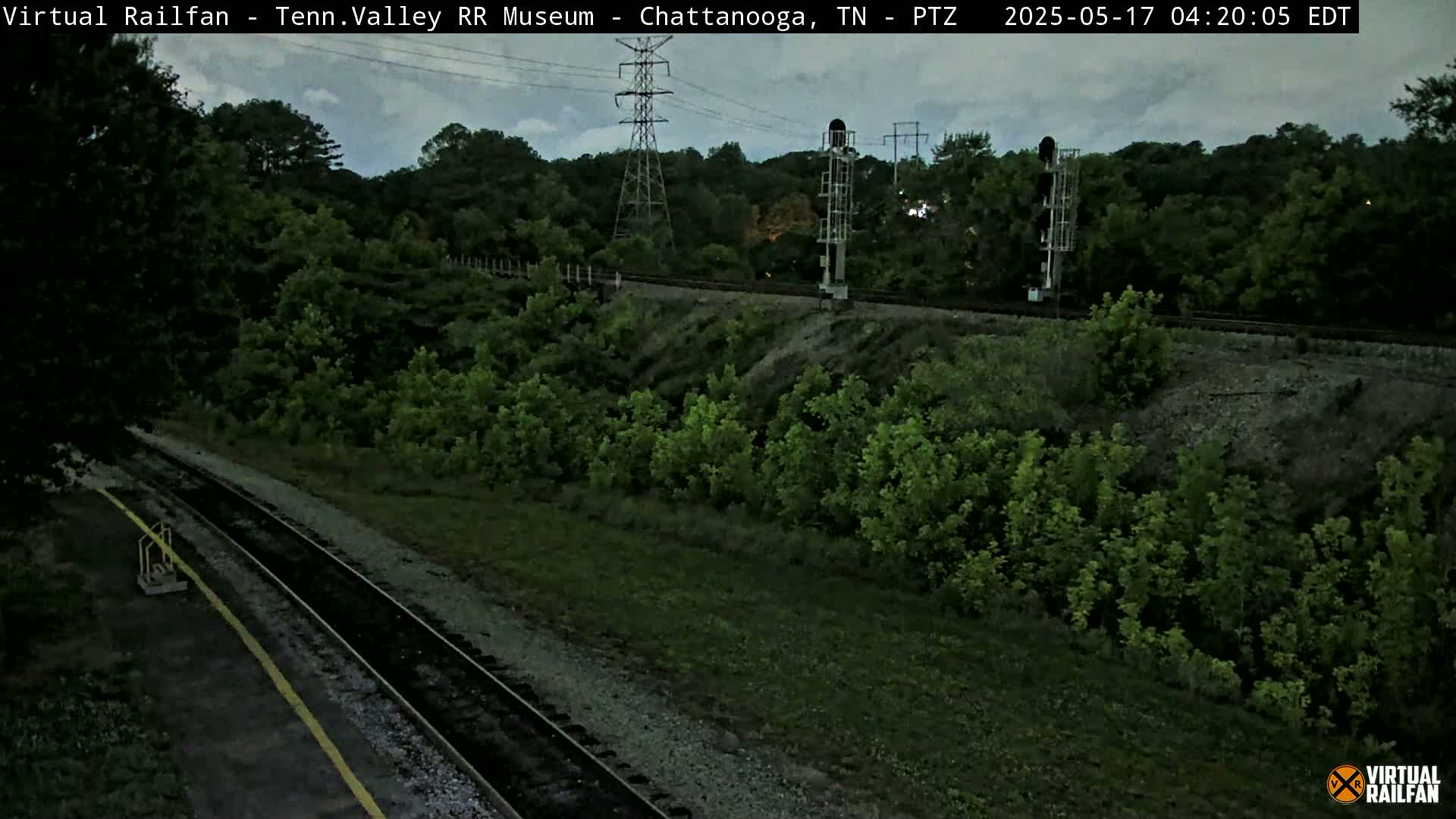 A high-angle, long shot shows a railway track winding through a verdant landscape under an overcast sky.