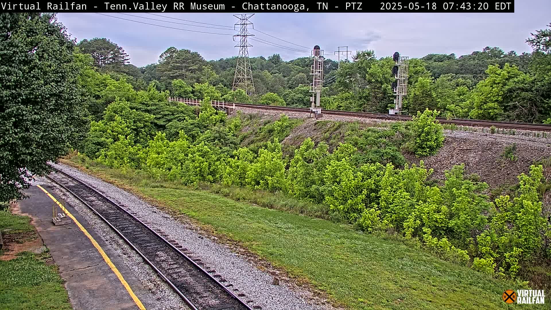 A high-angle view of railroad tracks running through a lush green landscape under an overcast sky.