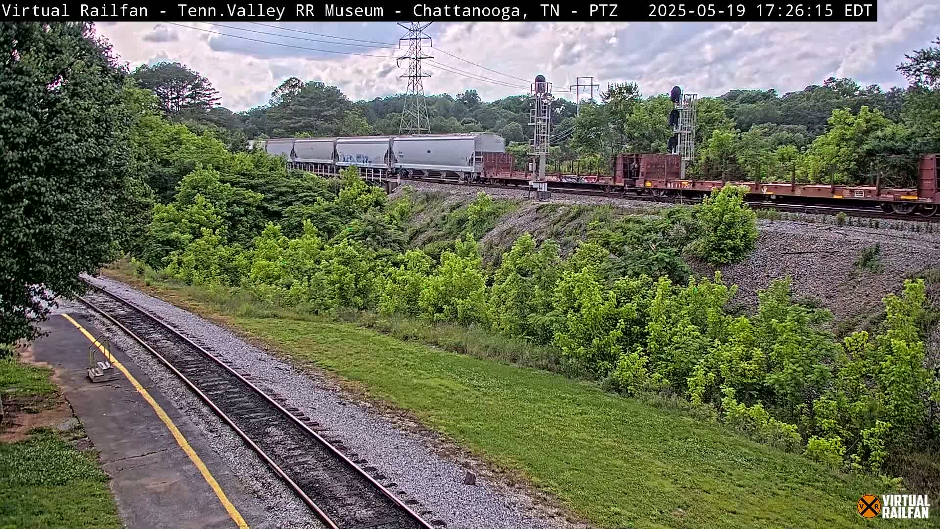 A freight train passes by a railway track on an overcast day, surrounded by lush green vegetation.