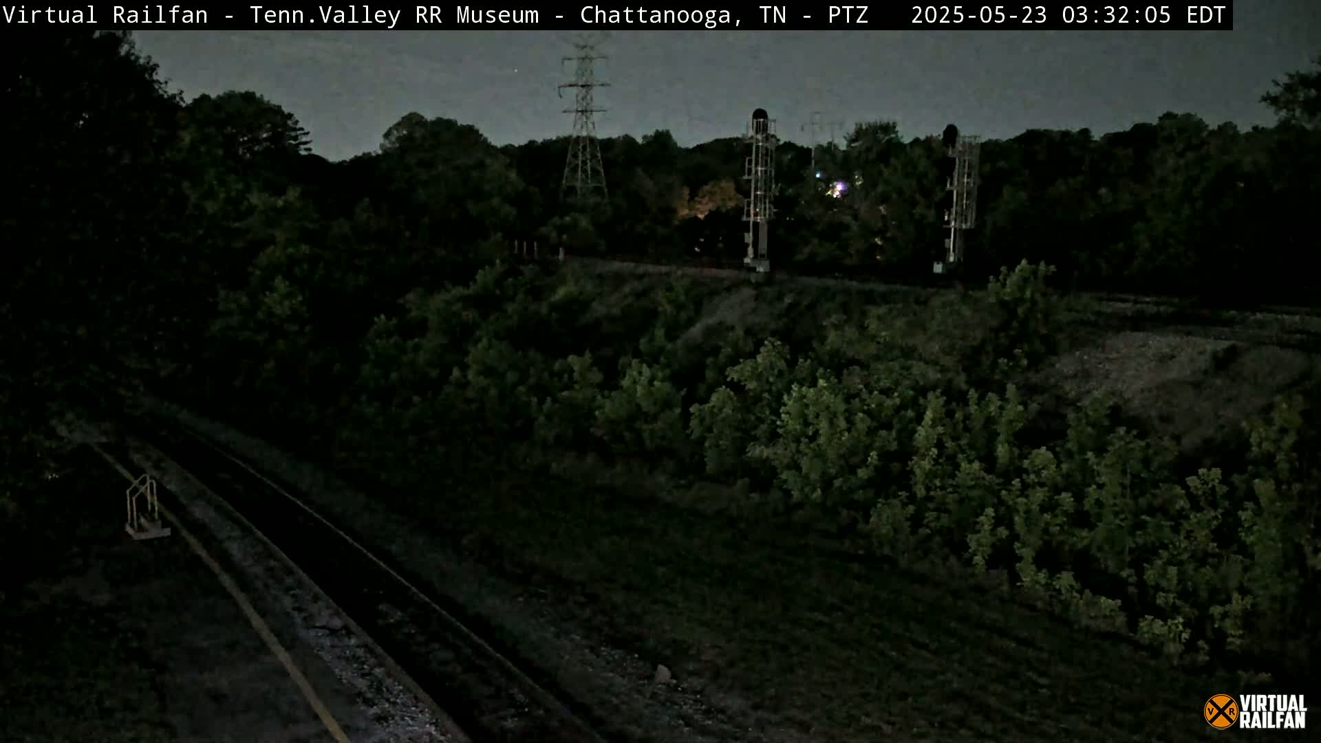 A nighttime view of a railroad track running through a dark, wooded area under a twilight sky.