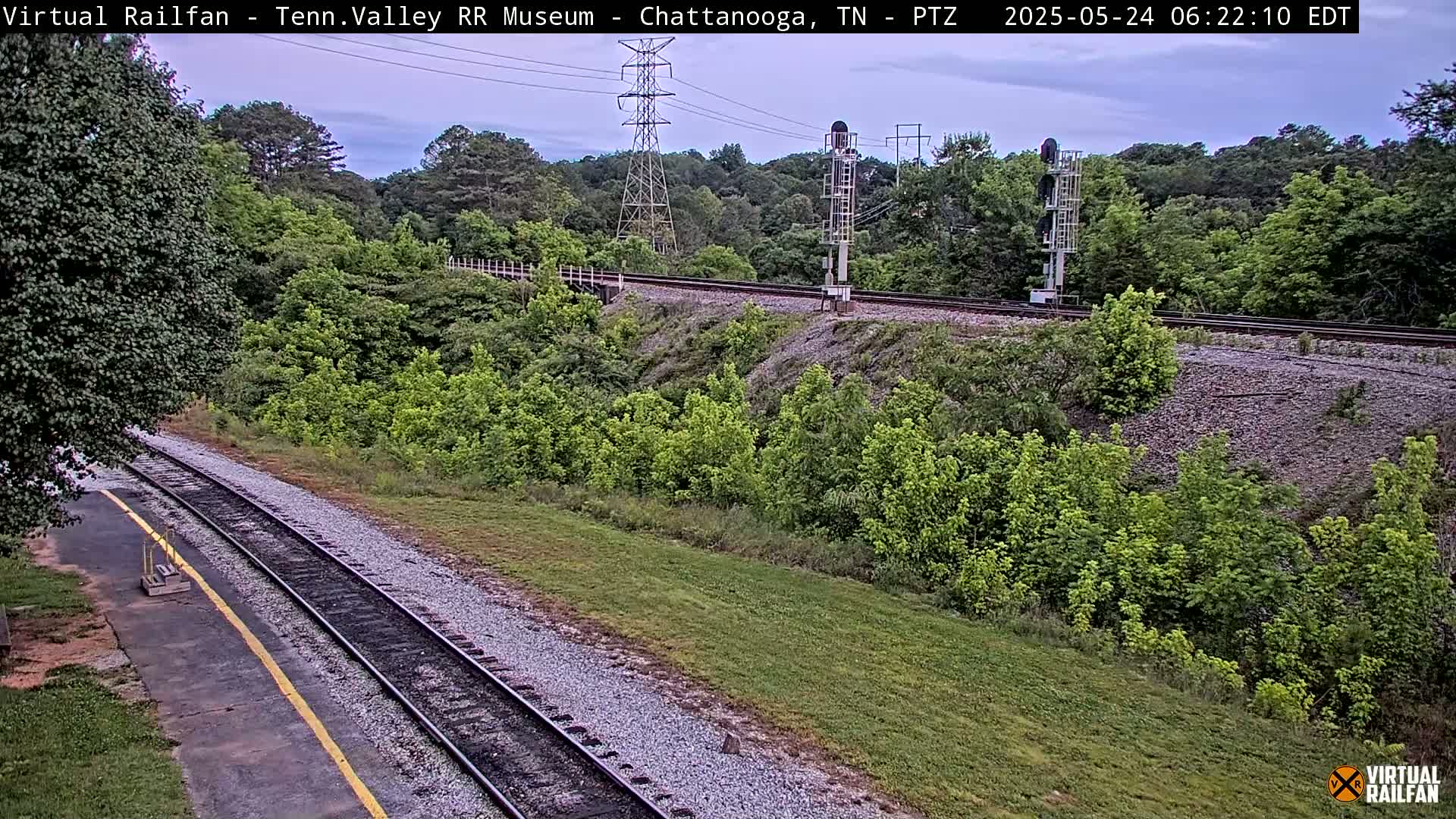 A high-angle, long shot of a railroad track winding through a lush, green landscape under an overcast sky.
