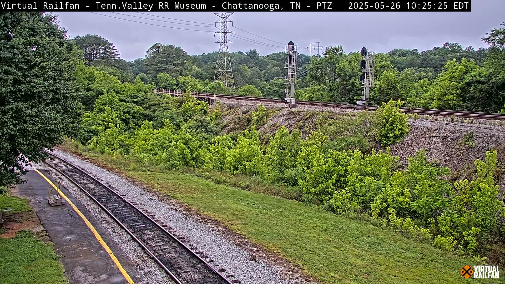 A railroad track winds through a lush green landscape under an overcast sky.
