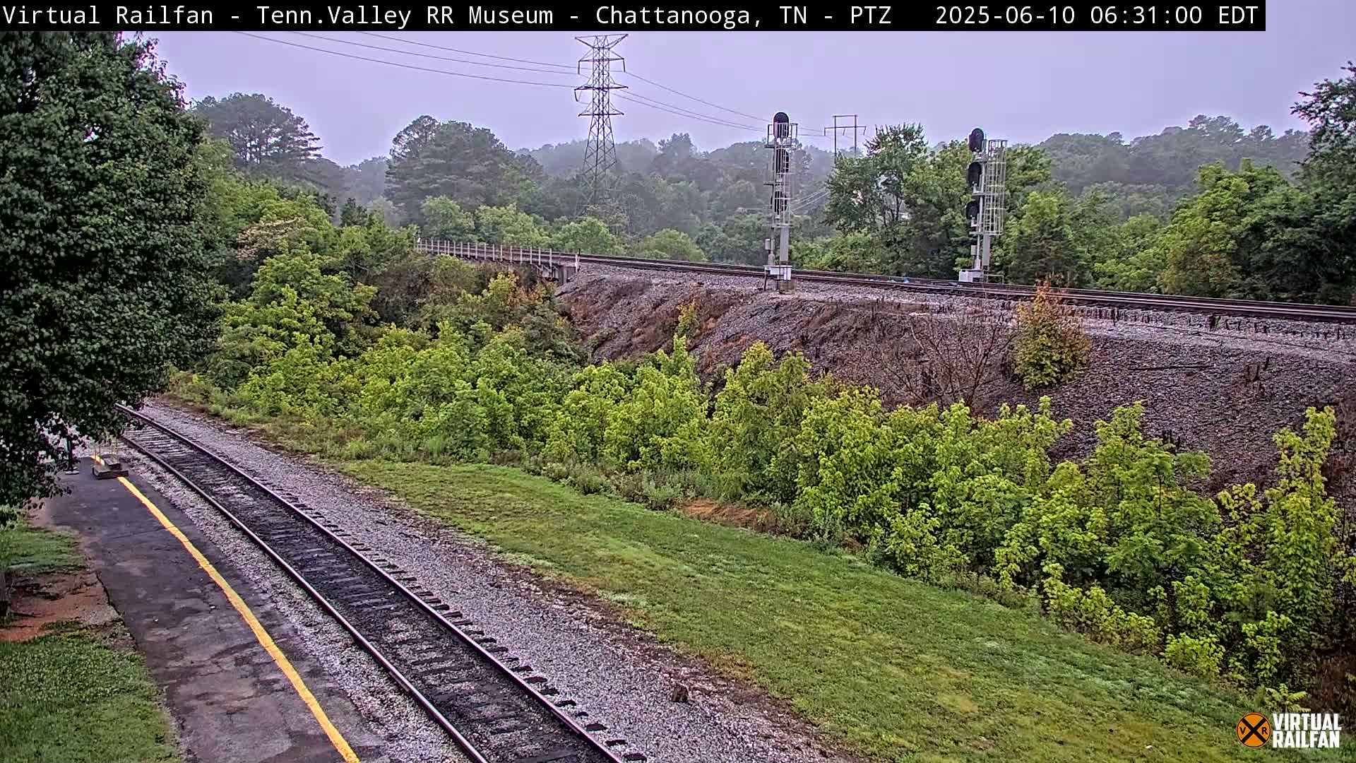 A view of a railway track winding through a lush green landscape under an overcast sky.