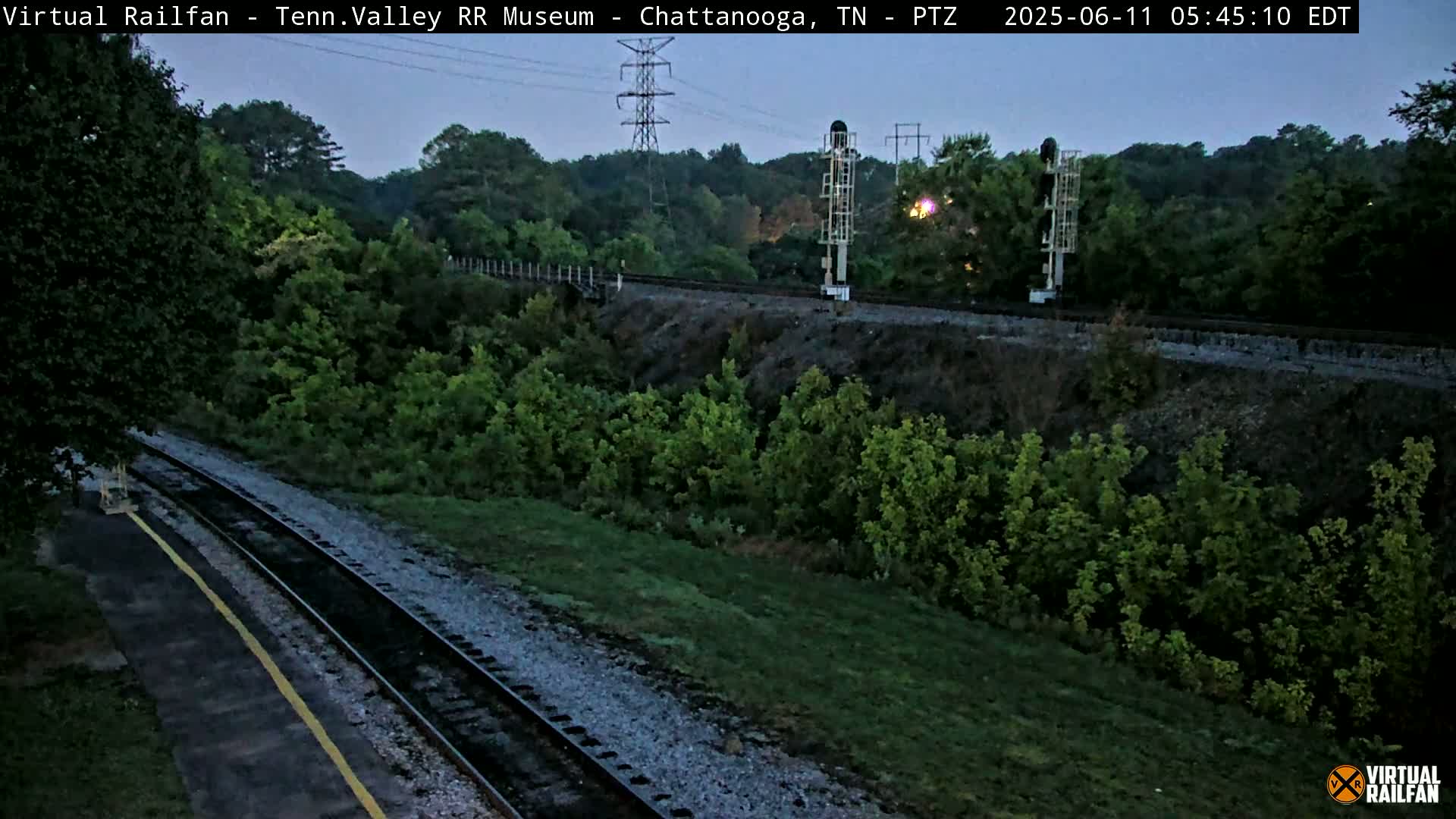 Railroad tracks wind through a lush green landscape under a twilight sky.