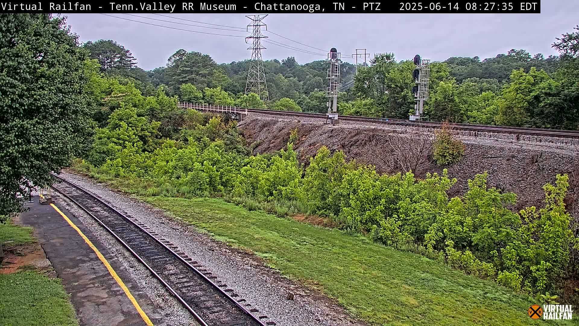 A high-angle view of a railroad track running through a lush green landscape under an overcast sky.