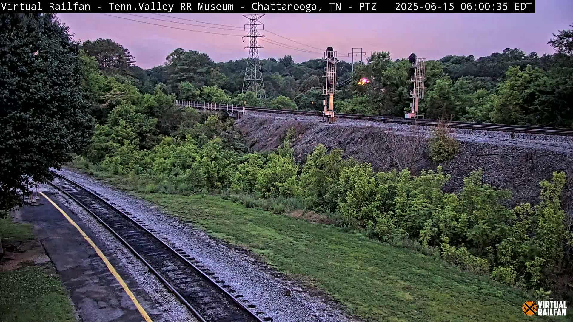 Railroad tracks wind through a verdant landscape under a twilight sky.