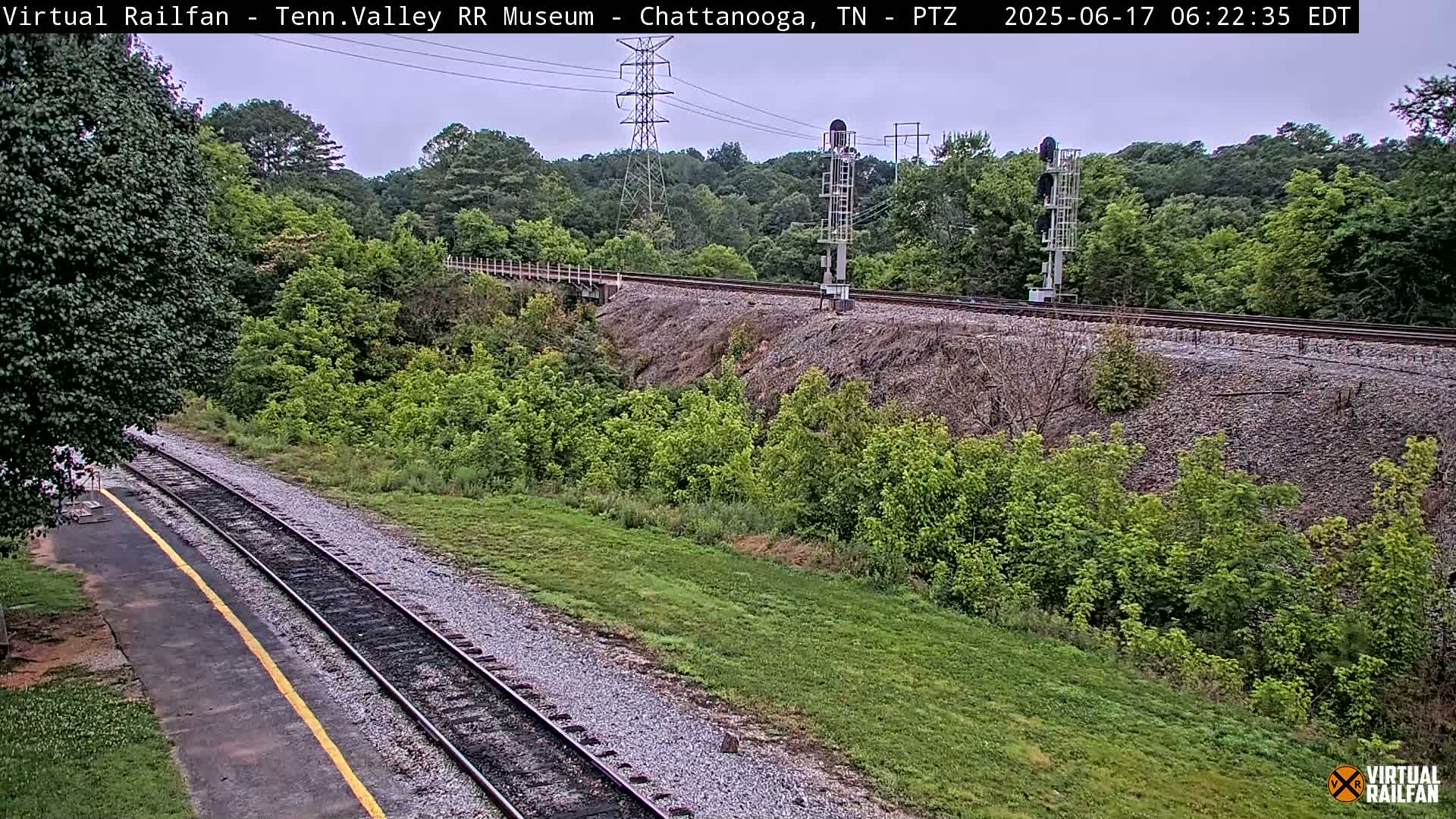 A railway track runs through a lush green landscape under an overcast sky.