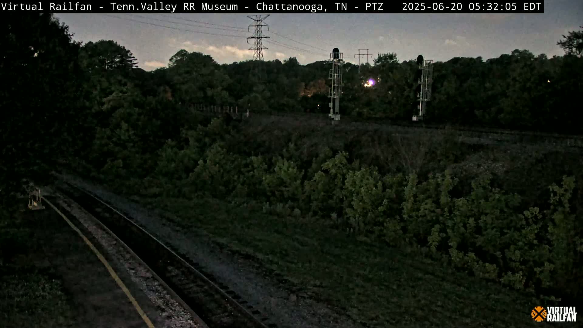 A nighttime view of train tracks running through a wooded area under a dusky sky.