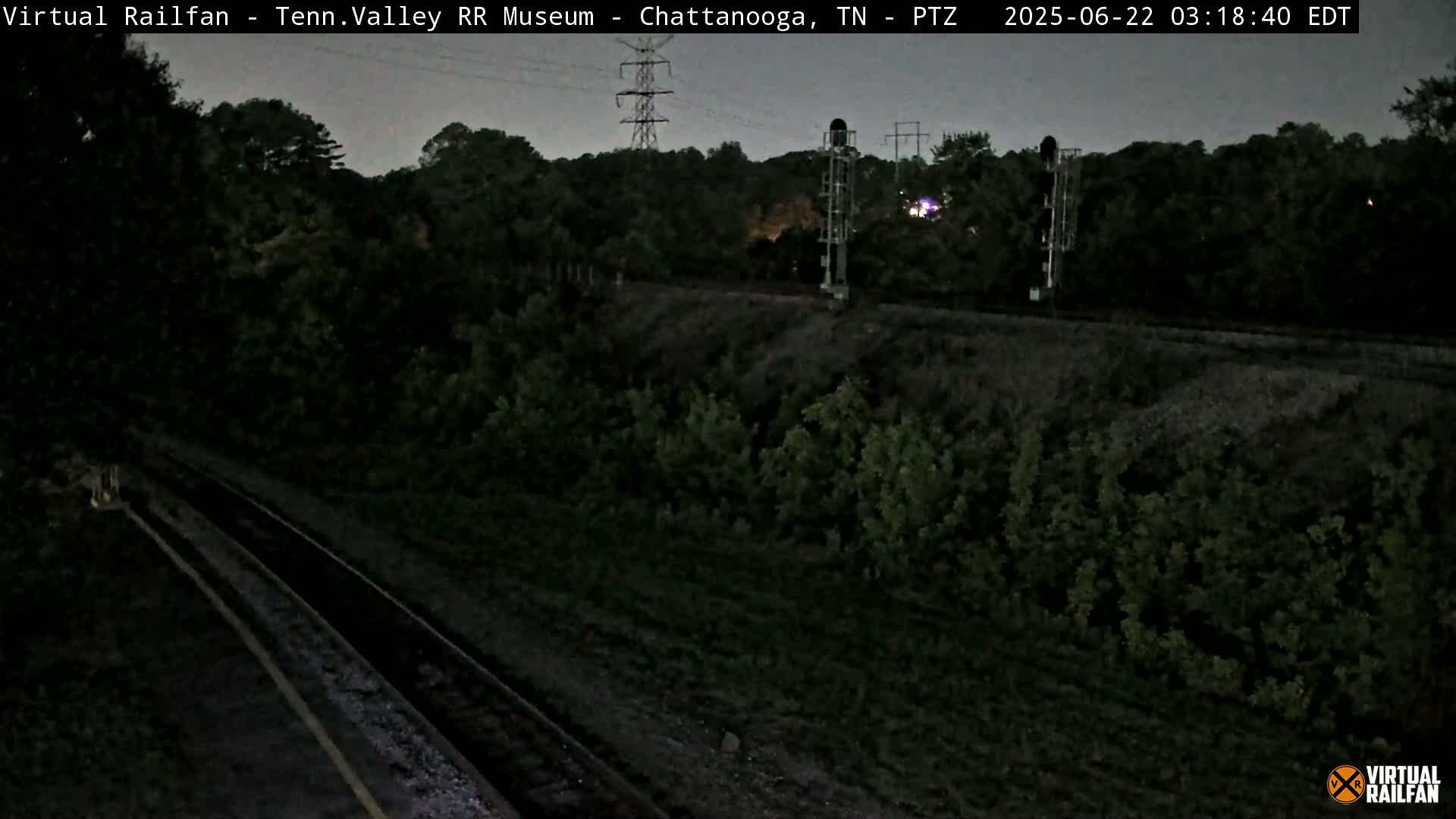 A nighttime view of railroad tracks running through a dark, wooded area under a twilight sky.