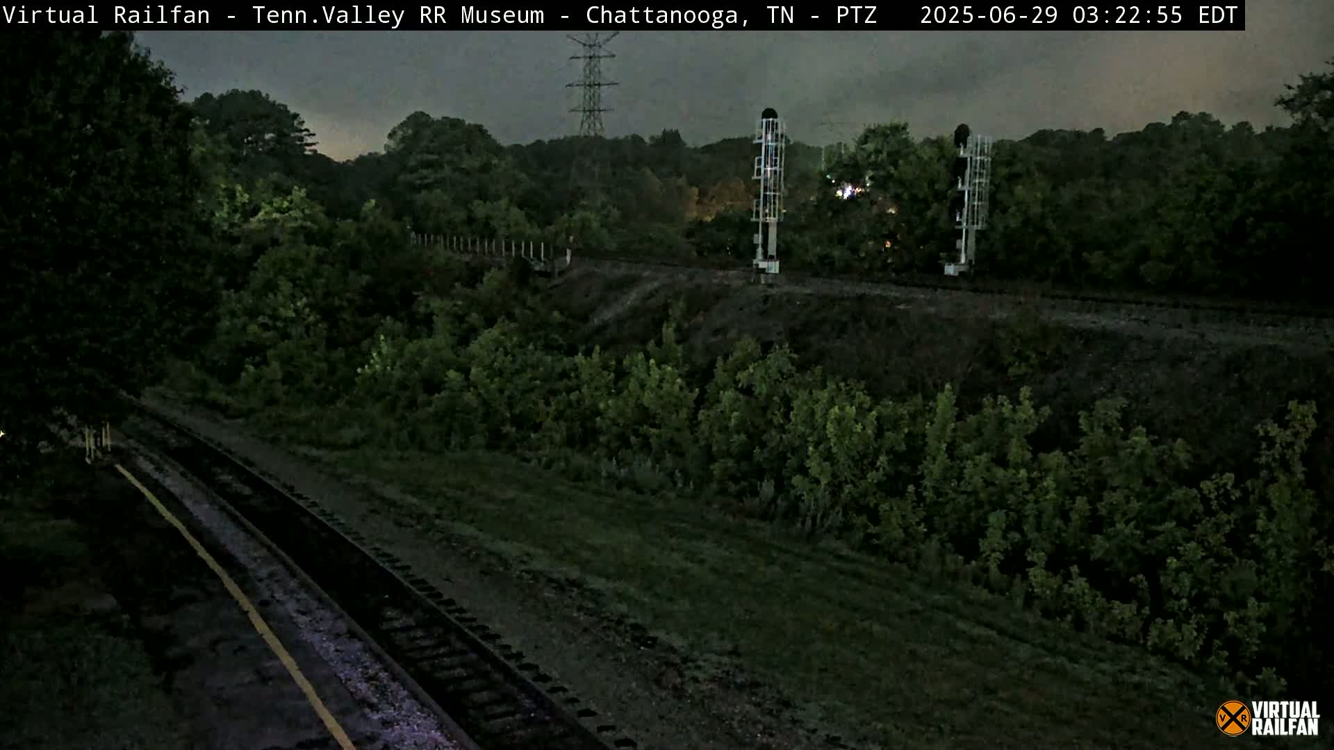 A nighttime view of train tracks that wind through a dark, lush green landscape under a cloudy sky.