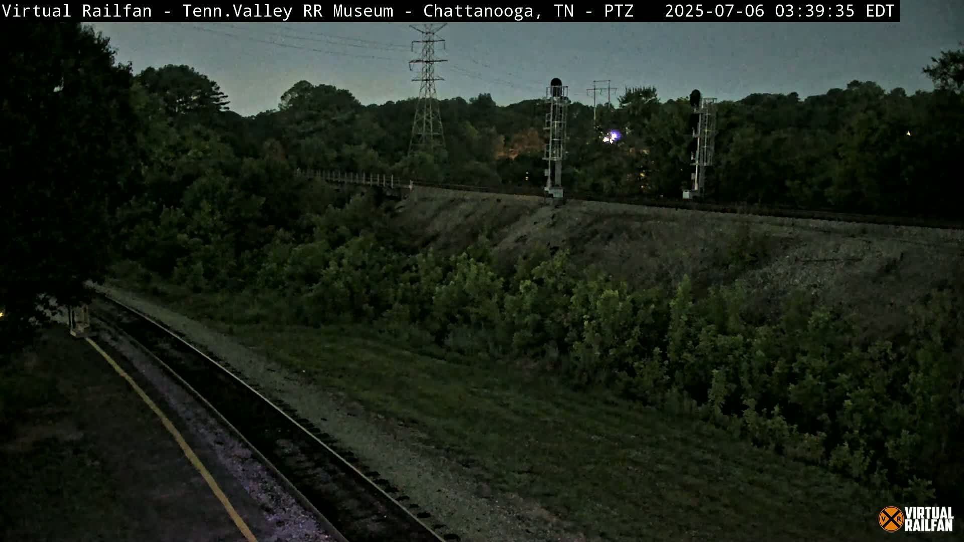 A nighttime view of railroad tracks running through a wooded area under a twilight sky.