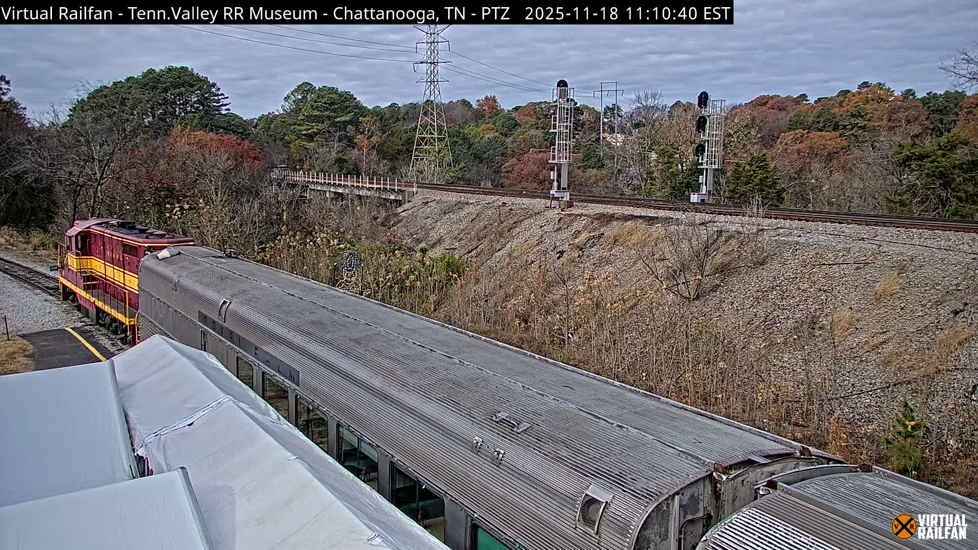 A high-angle, twilight view shows a railroad track winding through a lush green landscape, with power lines and signal equipment visible.