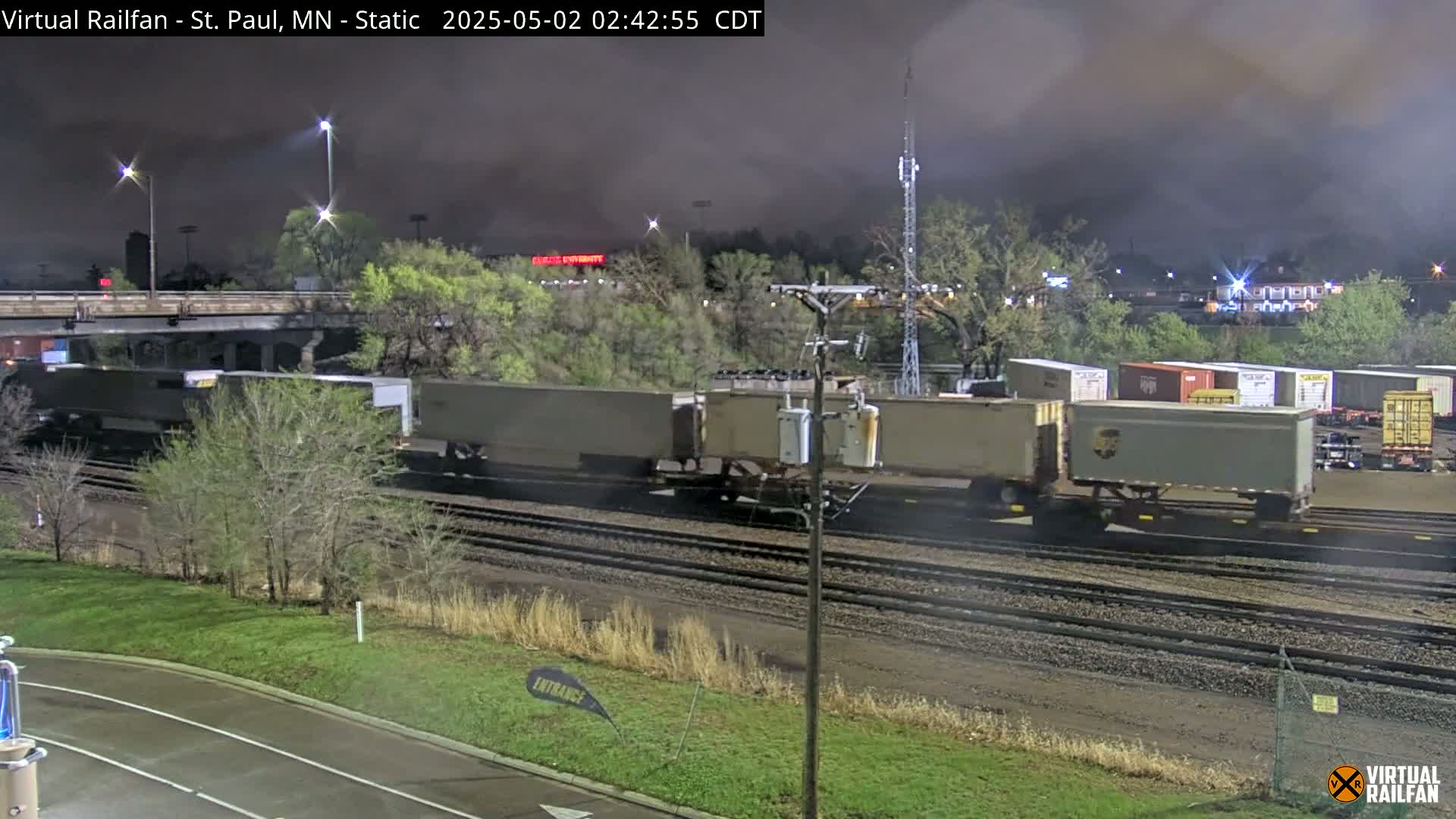 A long freight train sits on railway tracks under a dark, overcast night sky.