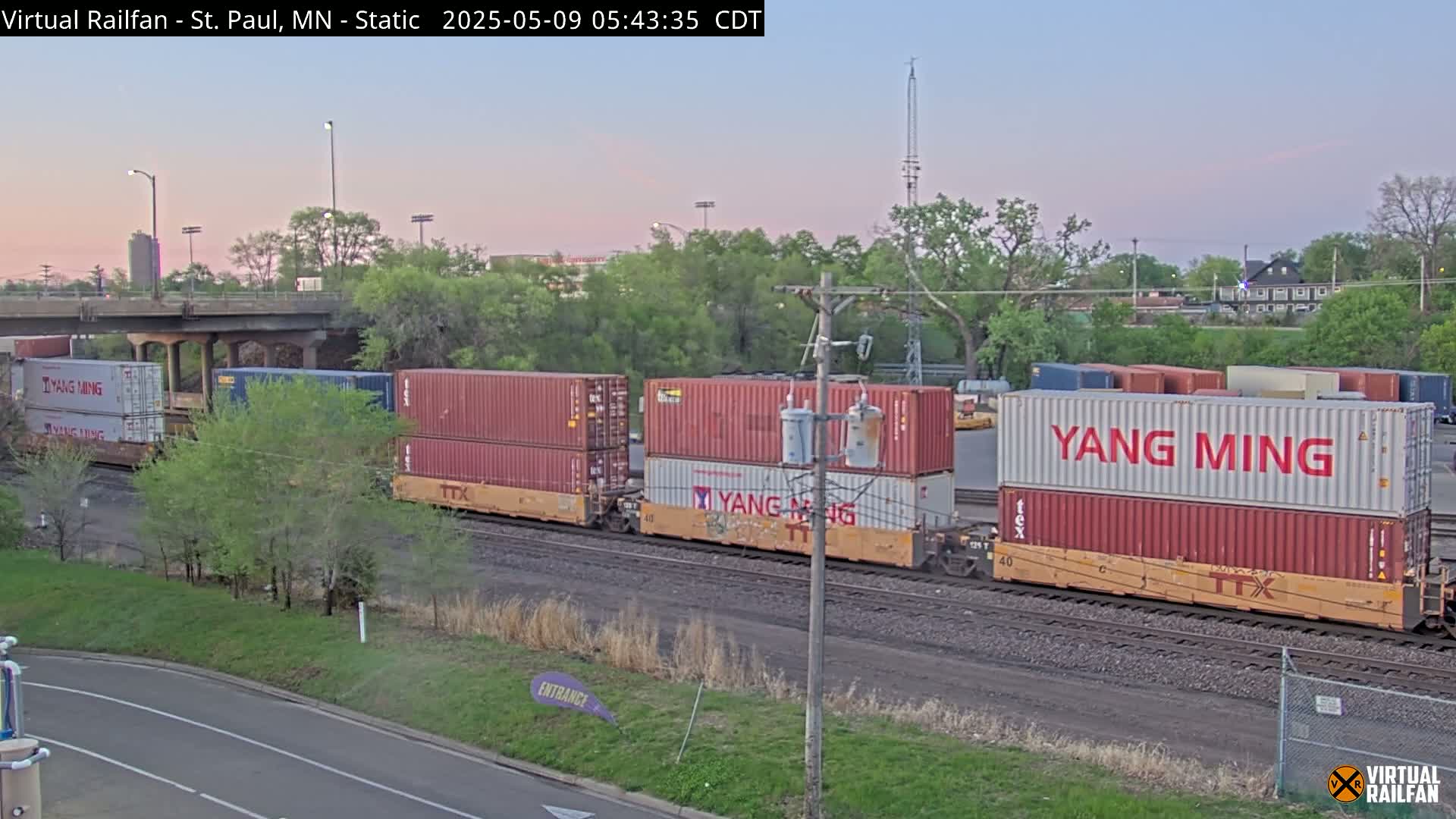 A freight train carrying multiple shipping containers, some marked "Yang Ming," sits on railway tracks under a twilight sky.