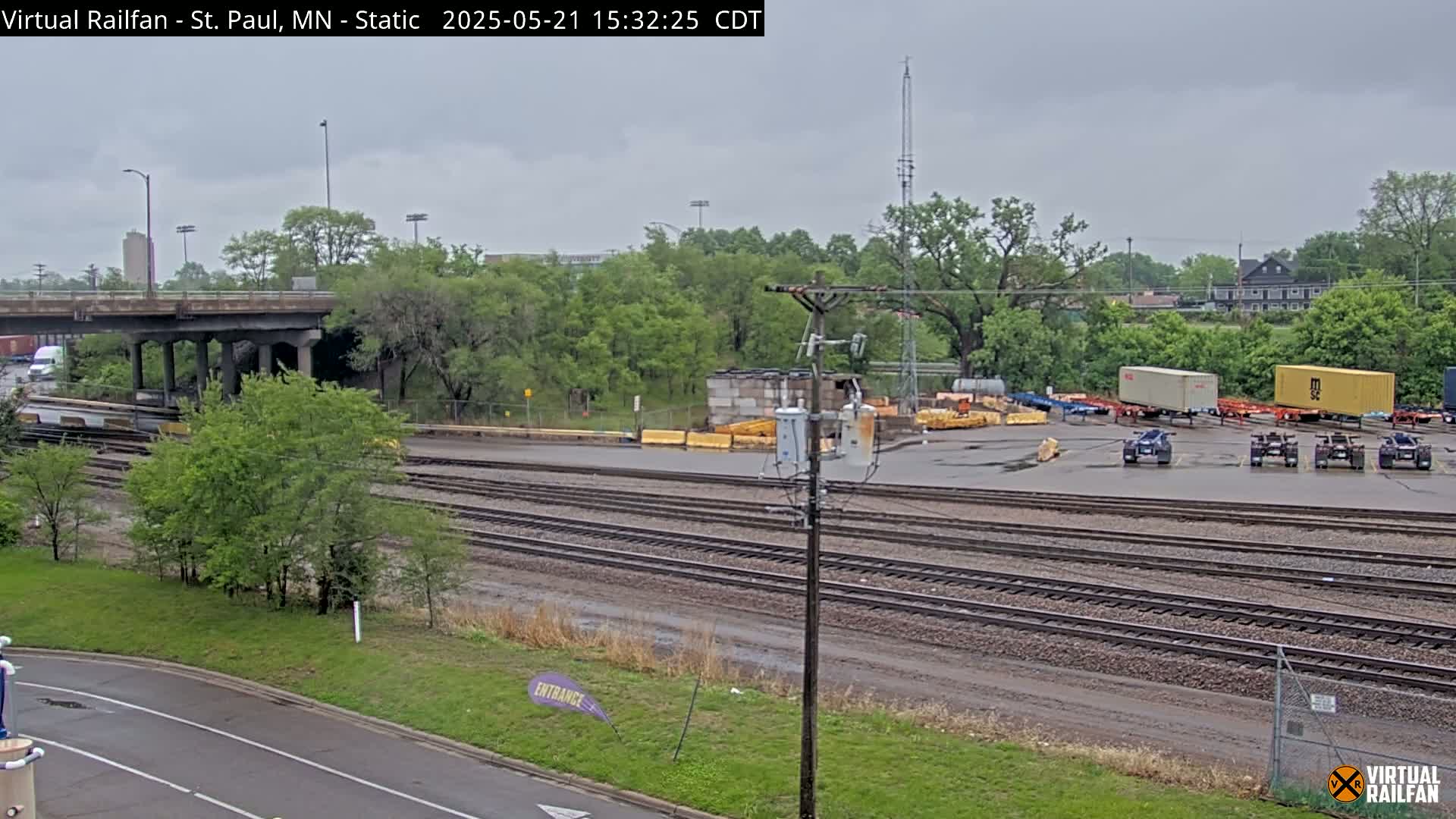 A railroad yard with several shipping containers and vehicles under an overcast sky.