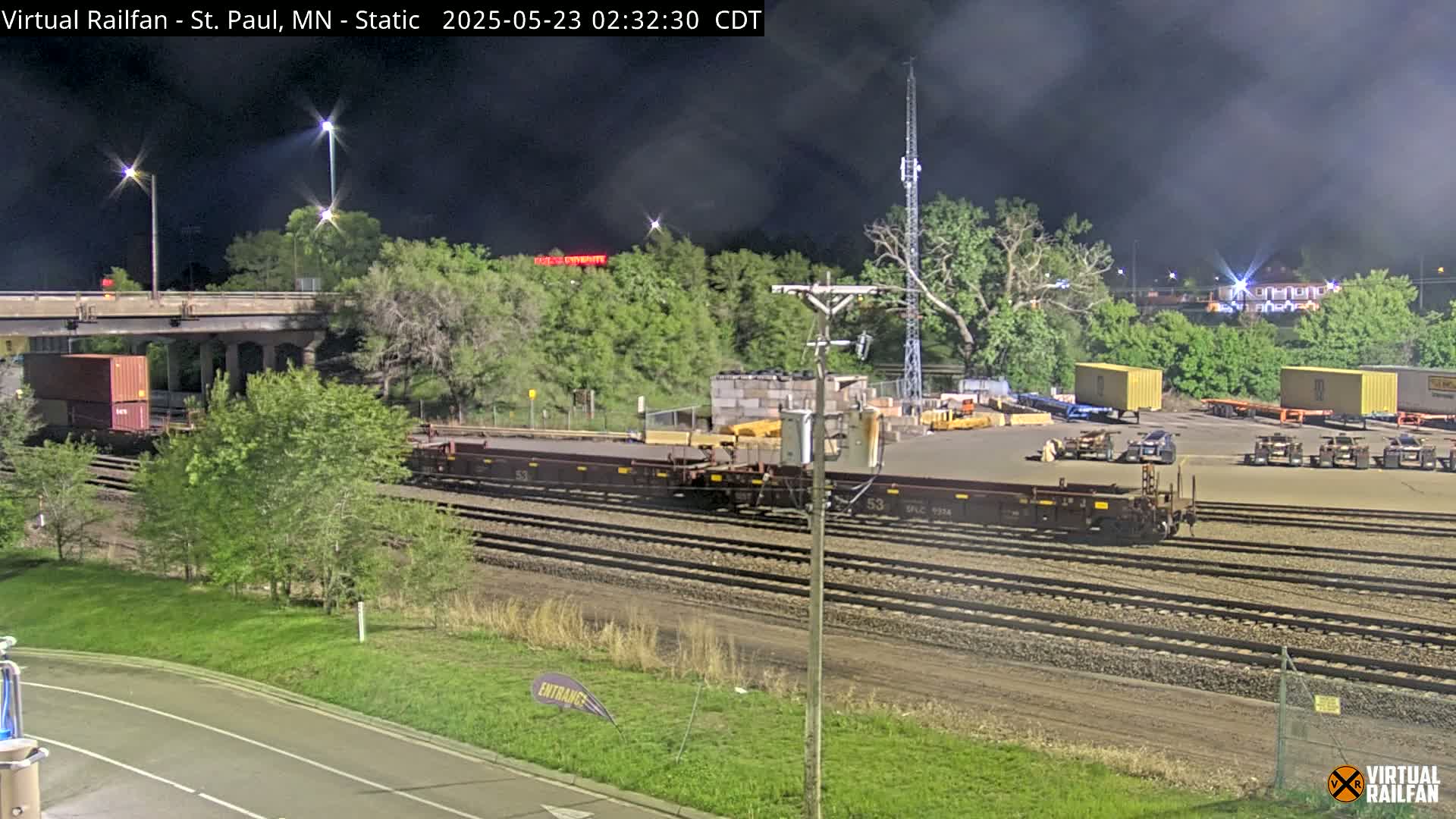 A nighttime view of a rail yard with several freight cars and containers, under a partly cloudy sky.