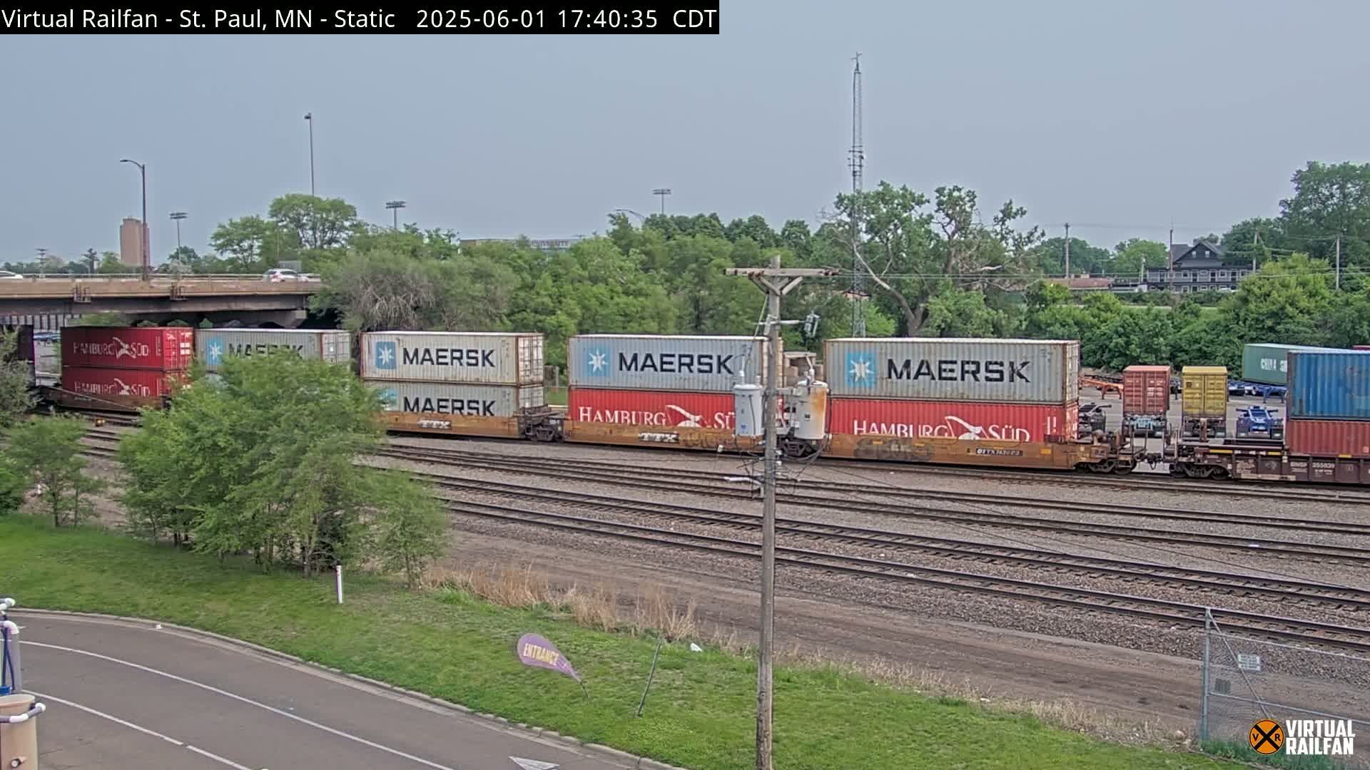 A freight train carrying multiple Maersk shipping containers sits on railroad tracks under an overcast sky.