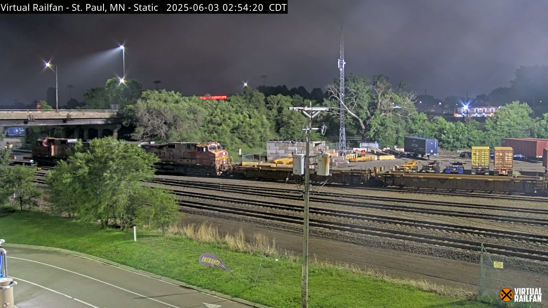 A nighttime view of a train yard with two locomotives and several freight cars under a dark, cloudy sky.
