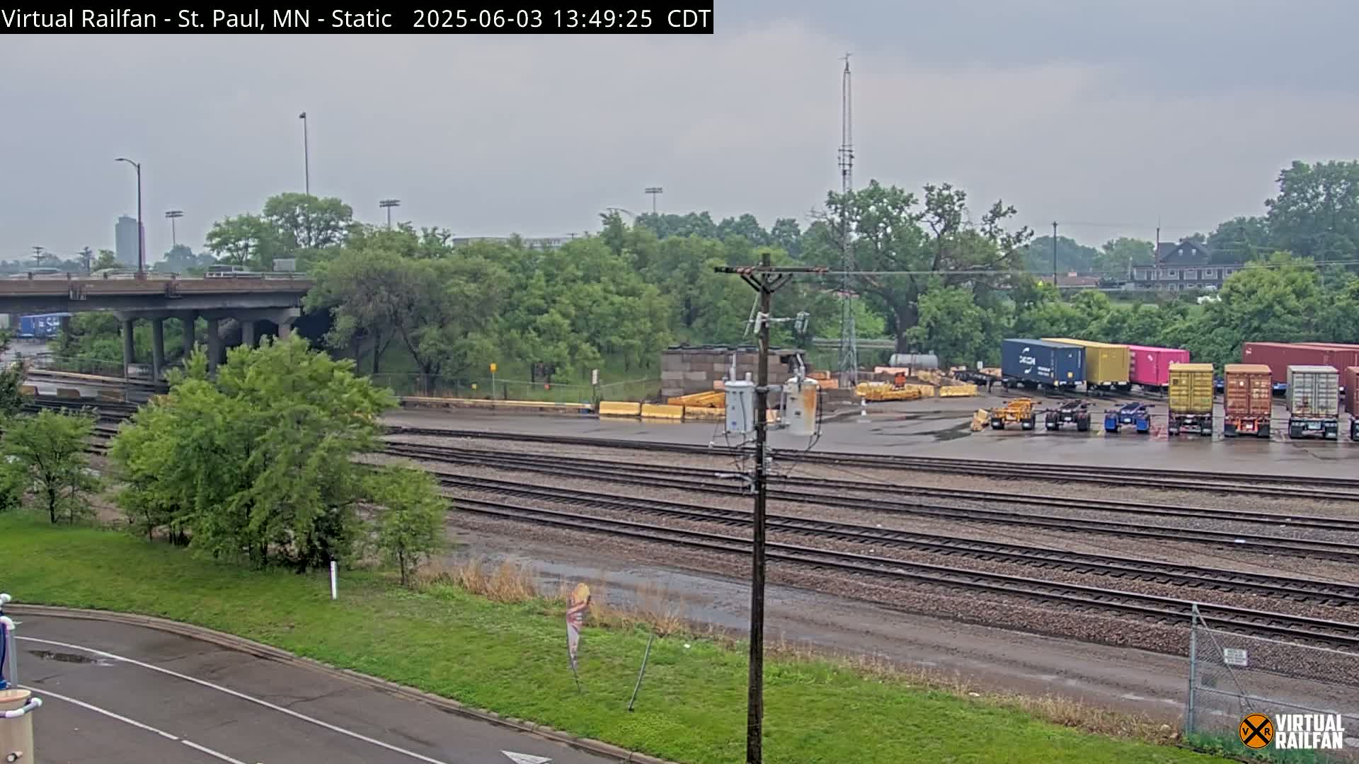 A railway yard with several shipping containers and train tracks under an overcast sky.