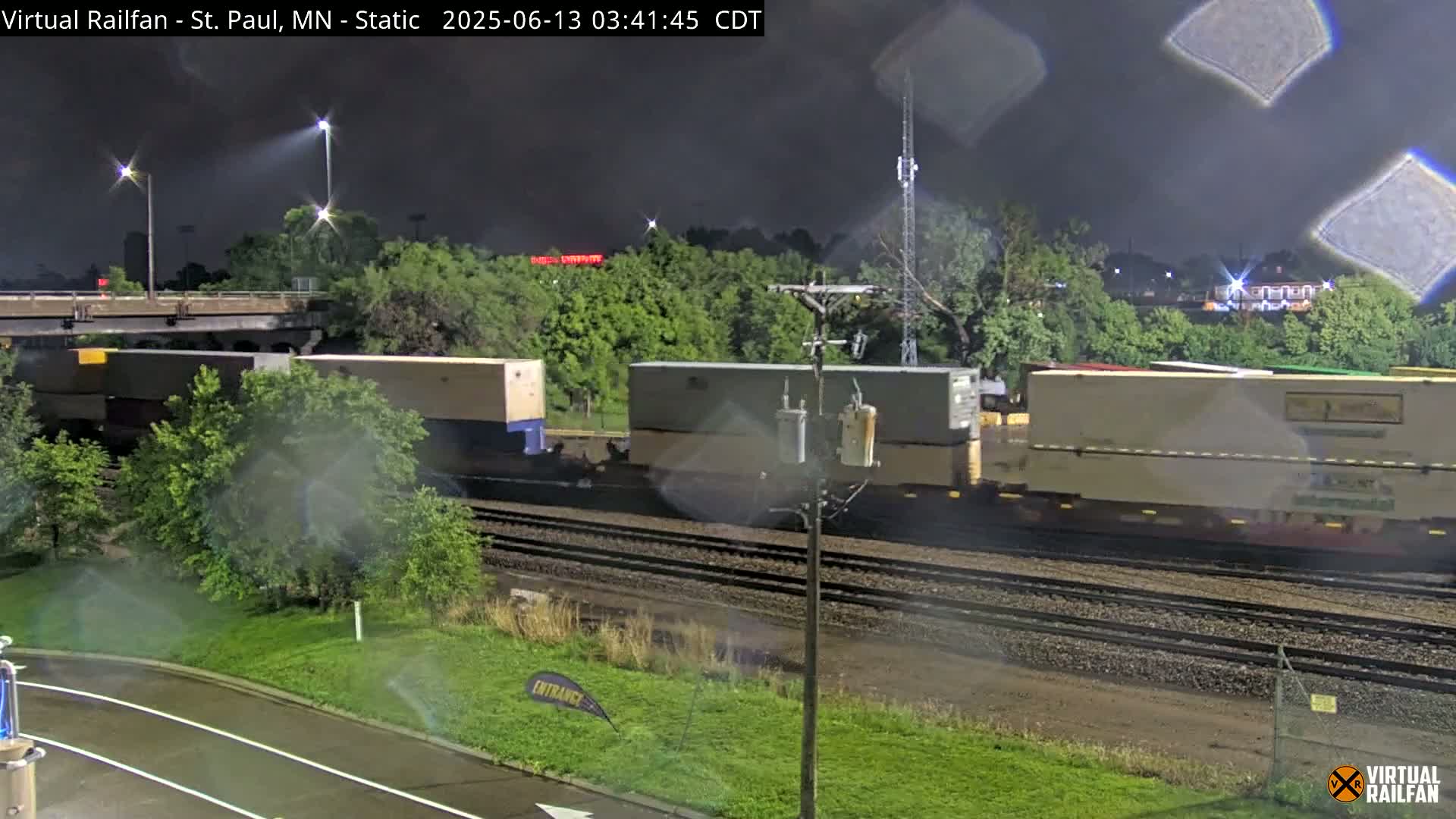 A nighttime view of a freight train on railway tracks under a dark, possibly rainy sky.