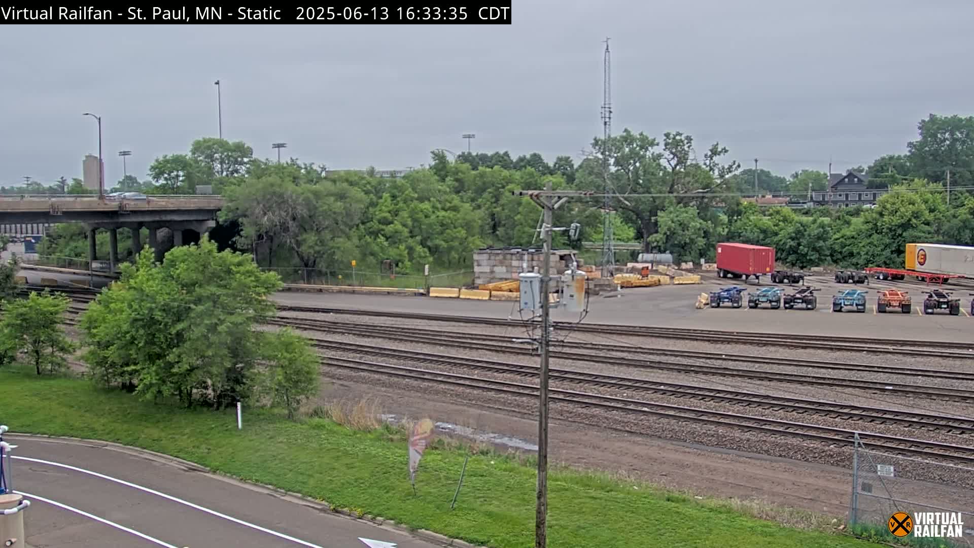 A view of railroad tracks and switching yards under an overcast sky, with several freight containers and other vehicles parked nearby.