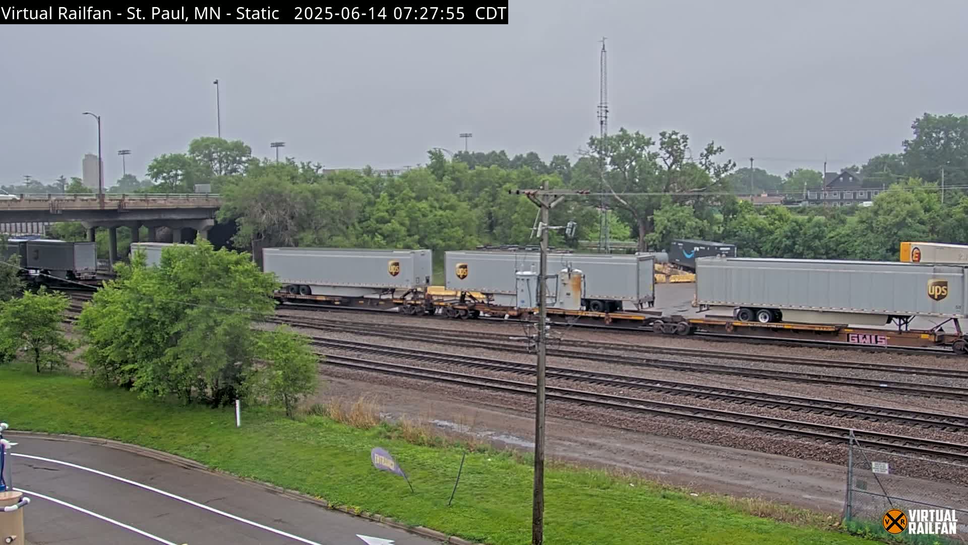A long freight train carrying several UPS containers sits on railway tracks under an overcast sky.