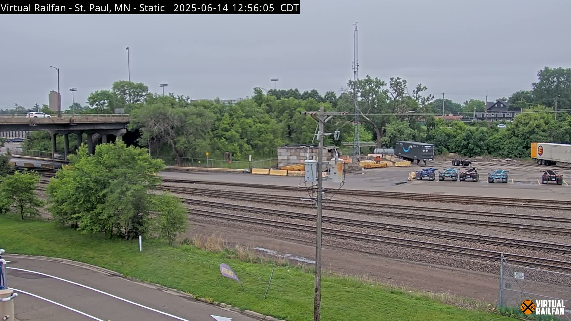 A railway yard with several rail lines, a road overpass, and various vehicles parked under an overcast sky.